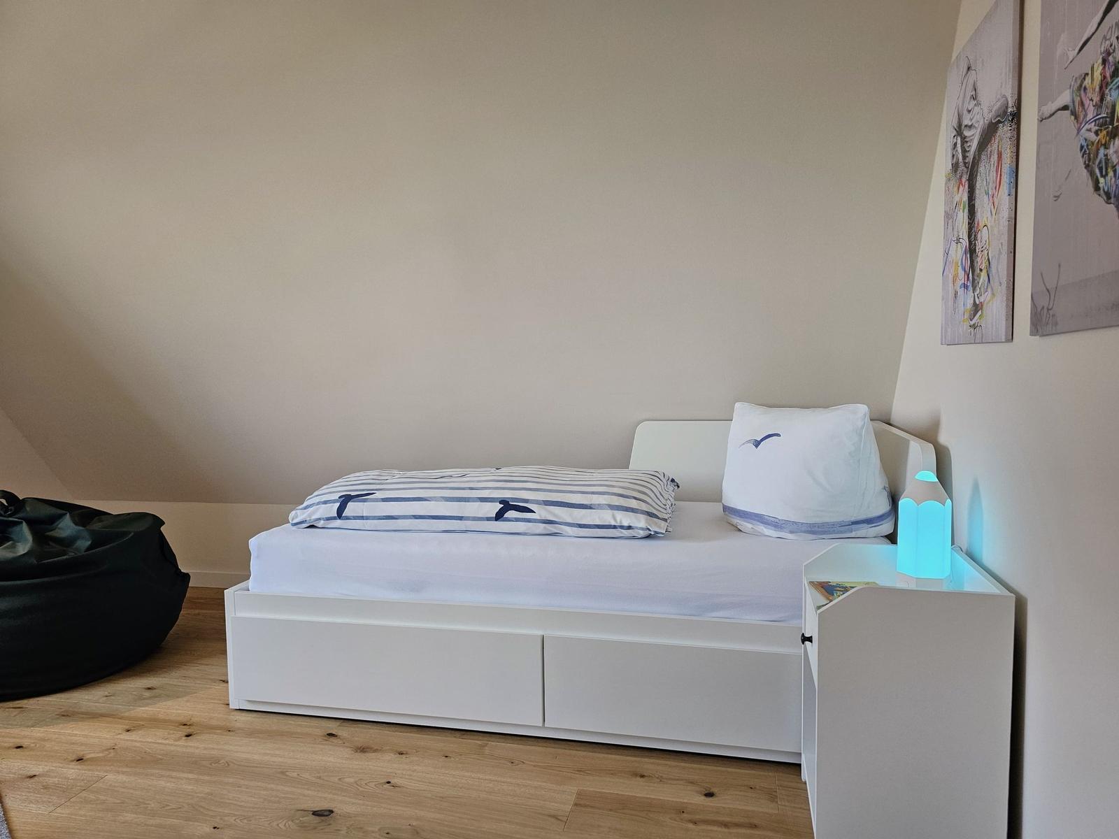 Schlafzimmer mit weißem Bett, Holzboden und Wandbildern