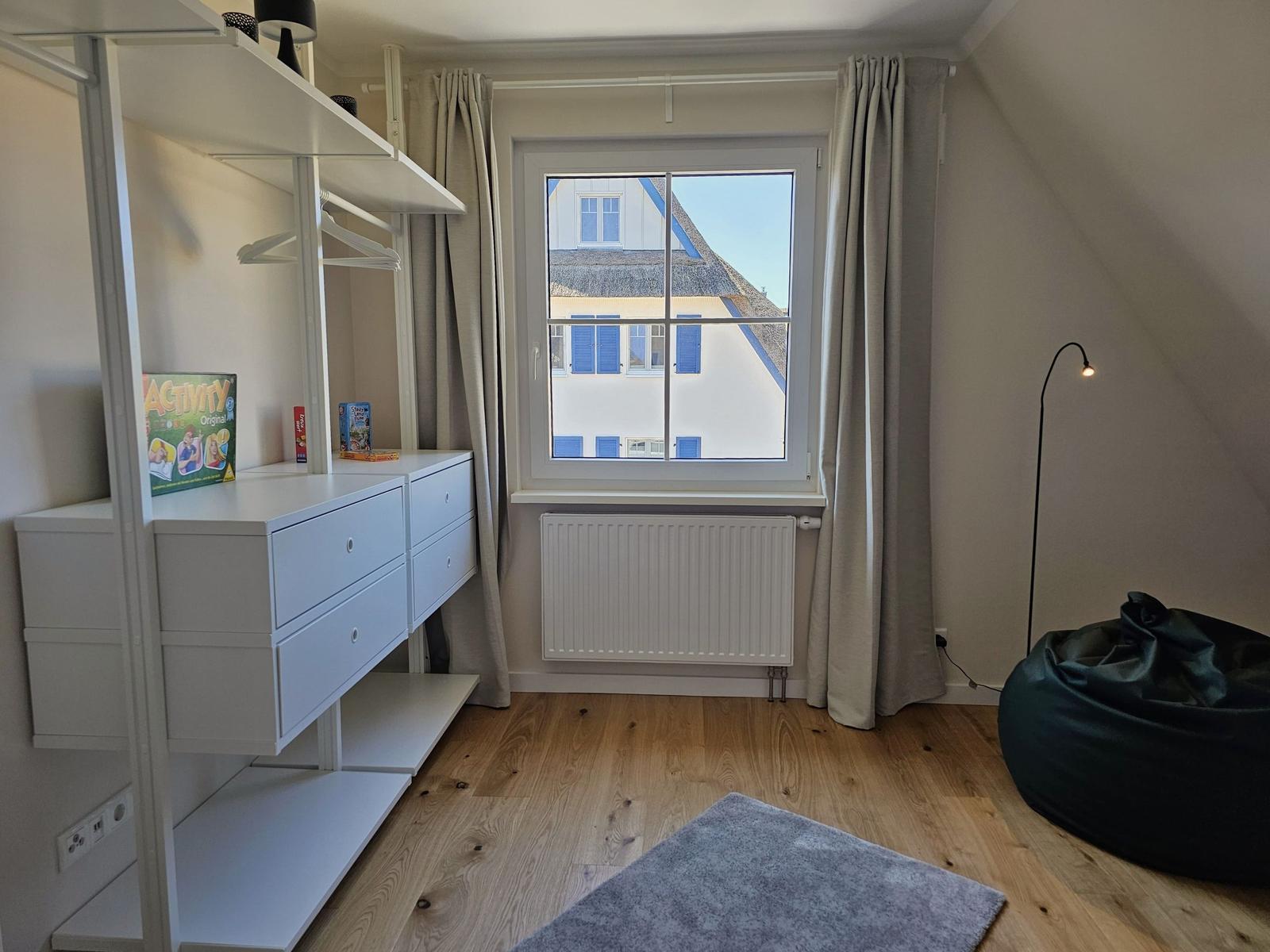Schlafzimmer mit Fenster, Kleiderschrank und Sitzgelegenheit.