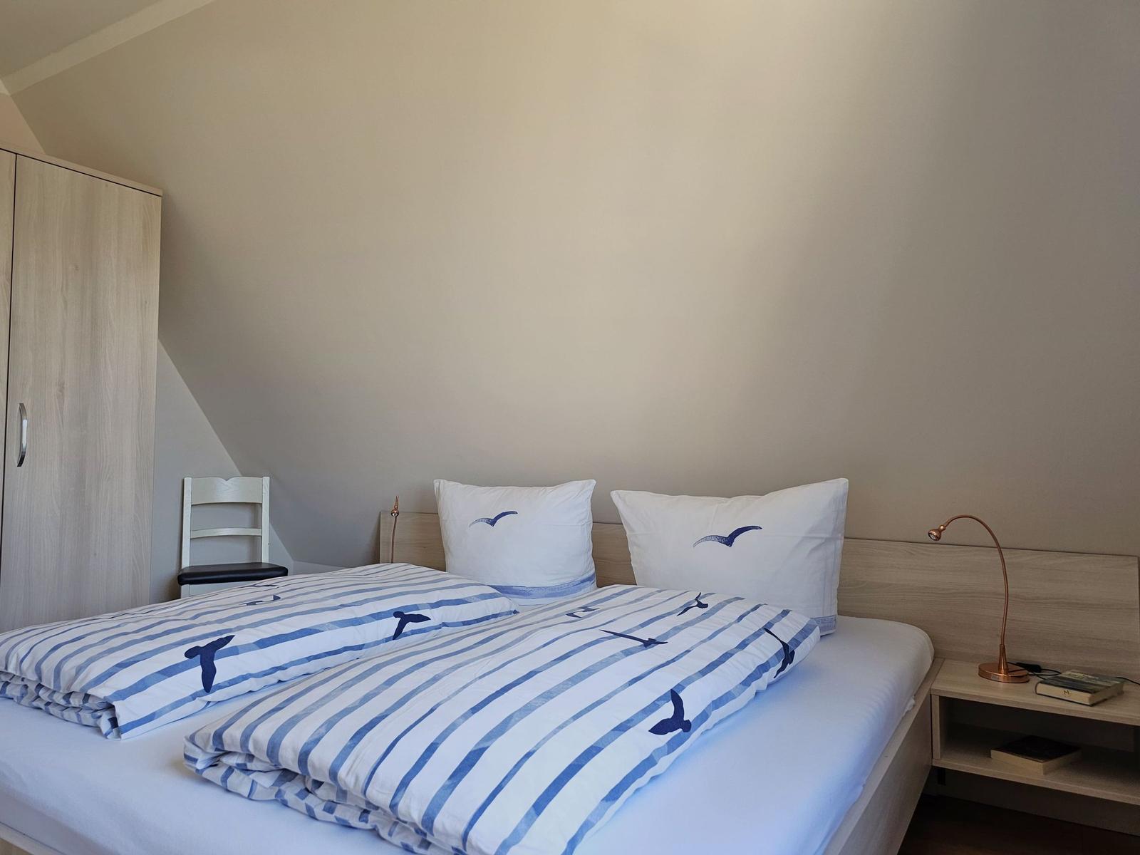 Schlafzimmer mit Doppelbett, Nachttisch und Kleiderschrank unter schrägem Dach