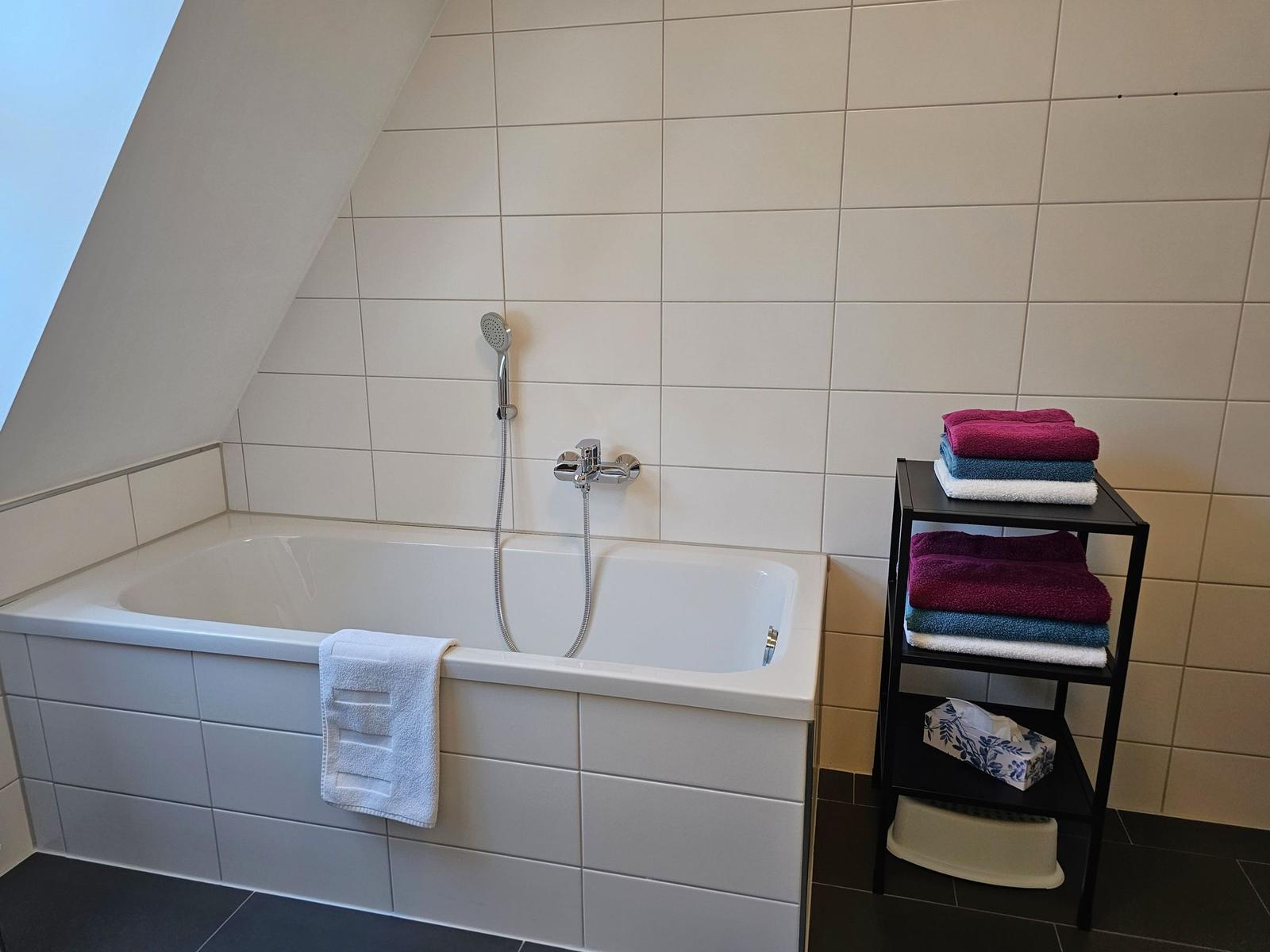 Bad mit Badewanne, Duschbrause und Handtuchständer.