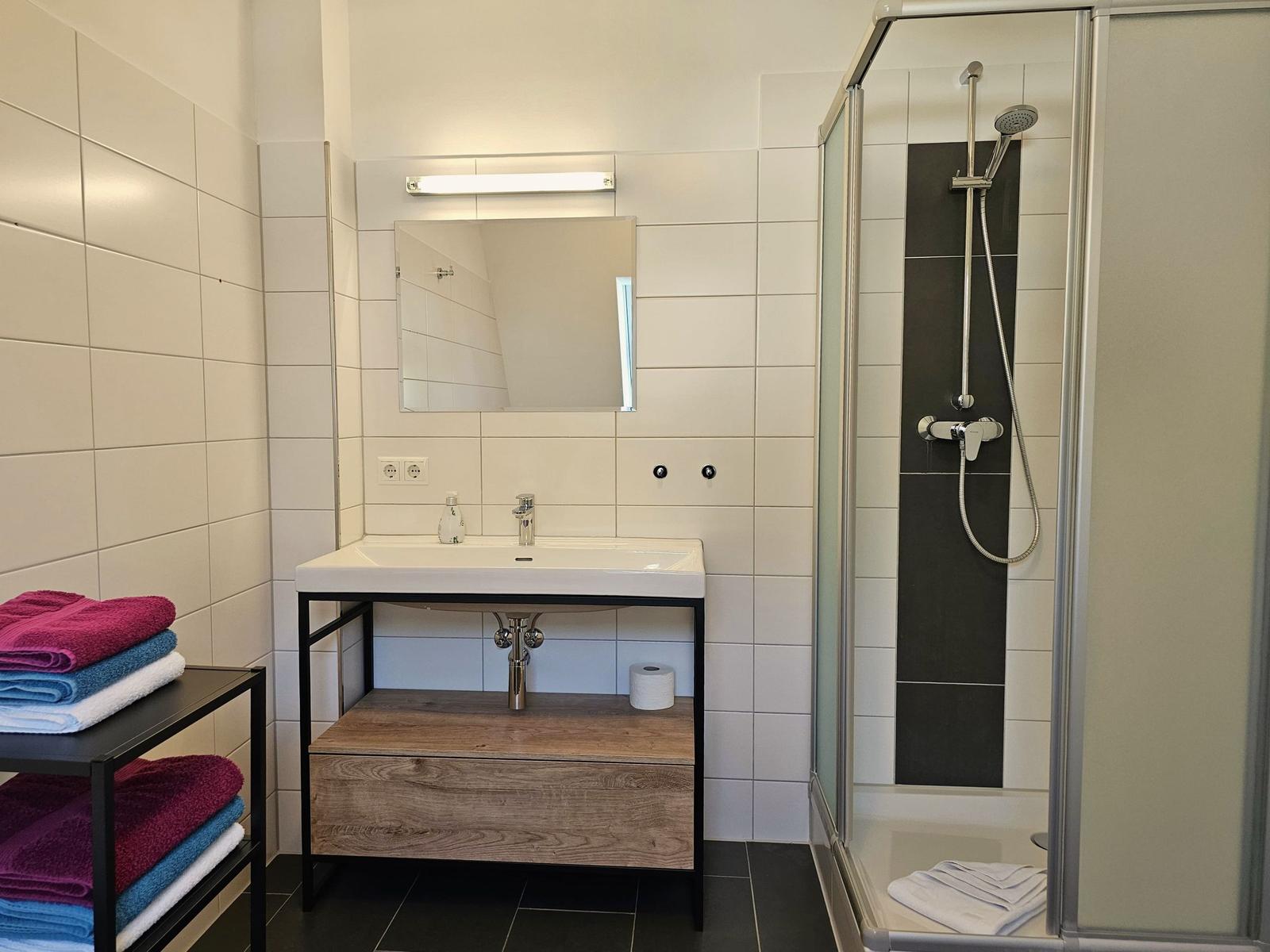 Badezimmer mit Dusche, Waschbecken und Handtüchern.