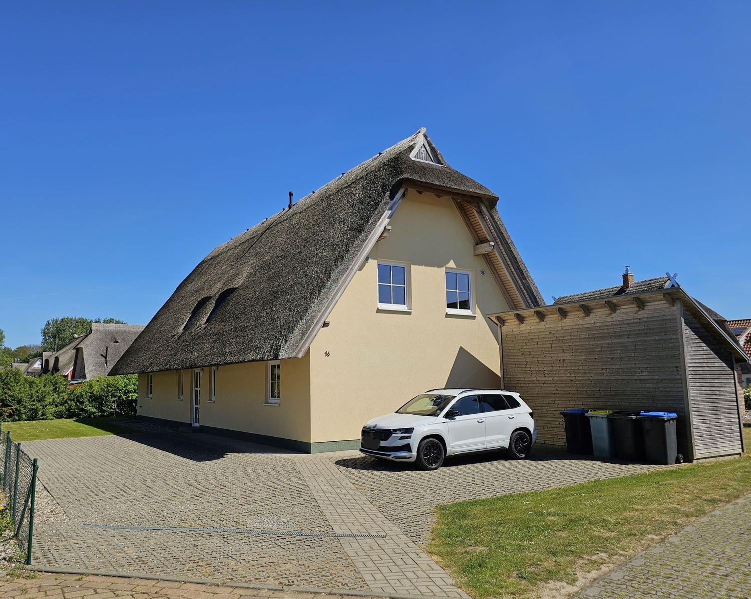 Haus mit Strohdach, gepflasterter Hof und weißem Auto.