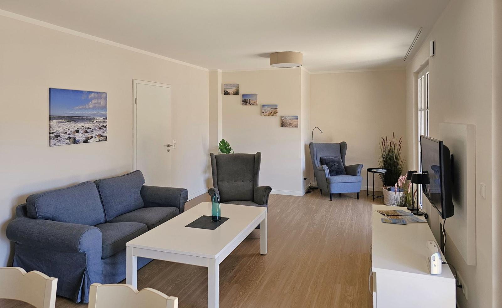 Wohnzimmer mit Sofa, Sessel und Fernseher an der Wand