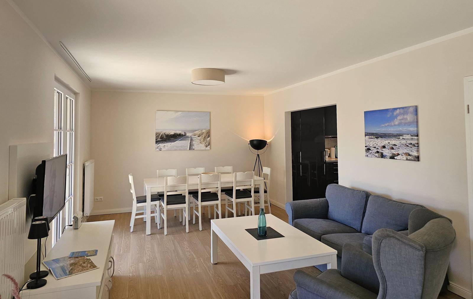 Wohn- und Essbereich mit Sofa, Tisch und Stühlen. Wandbilder zeigen Strand.