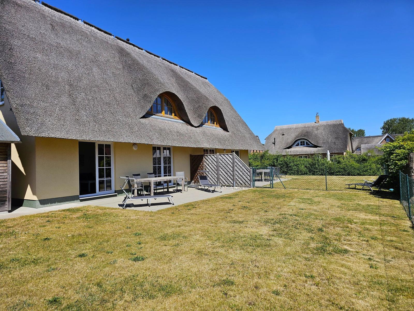 Haus mit Strohdach, Terrasse und Garten. Hinterhof mit Liegen und Tisch.