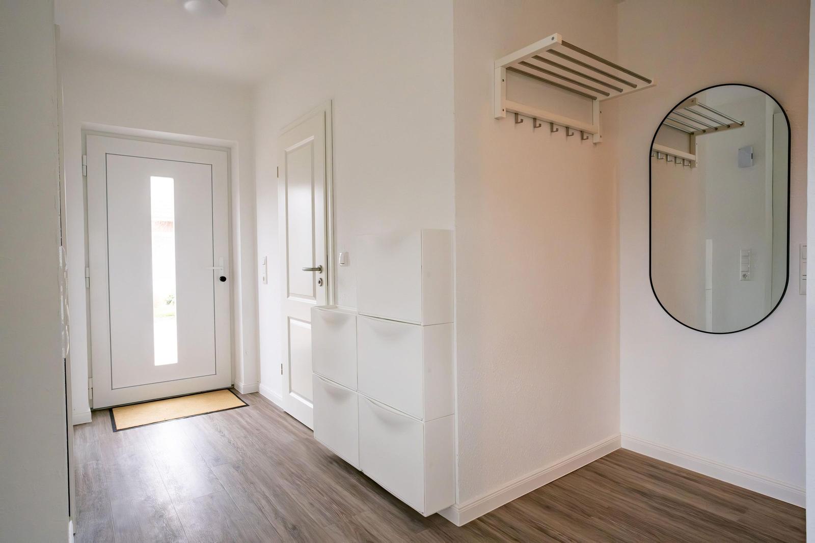 Eingangsbereich mit weißen Türen, Schuhschrank und runden Spiegel an der Wand.