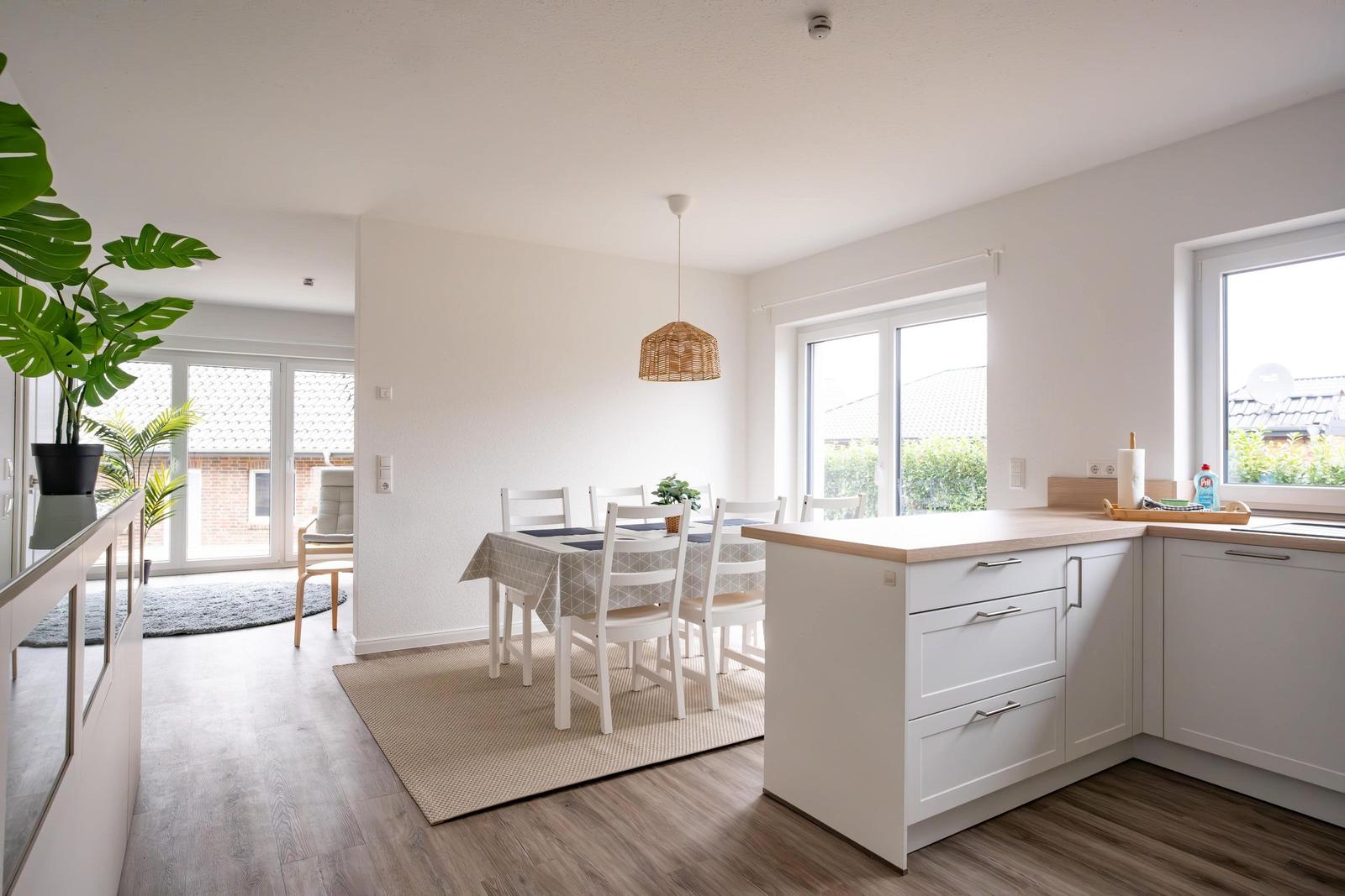 Küche mit Essbereich, weiße Schränke, Holzoberfläche und Fenster.