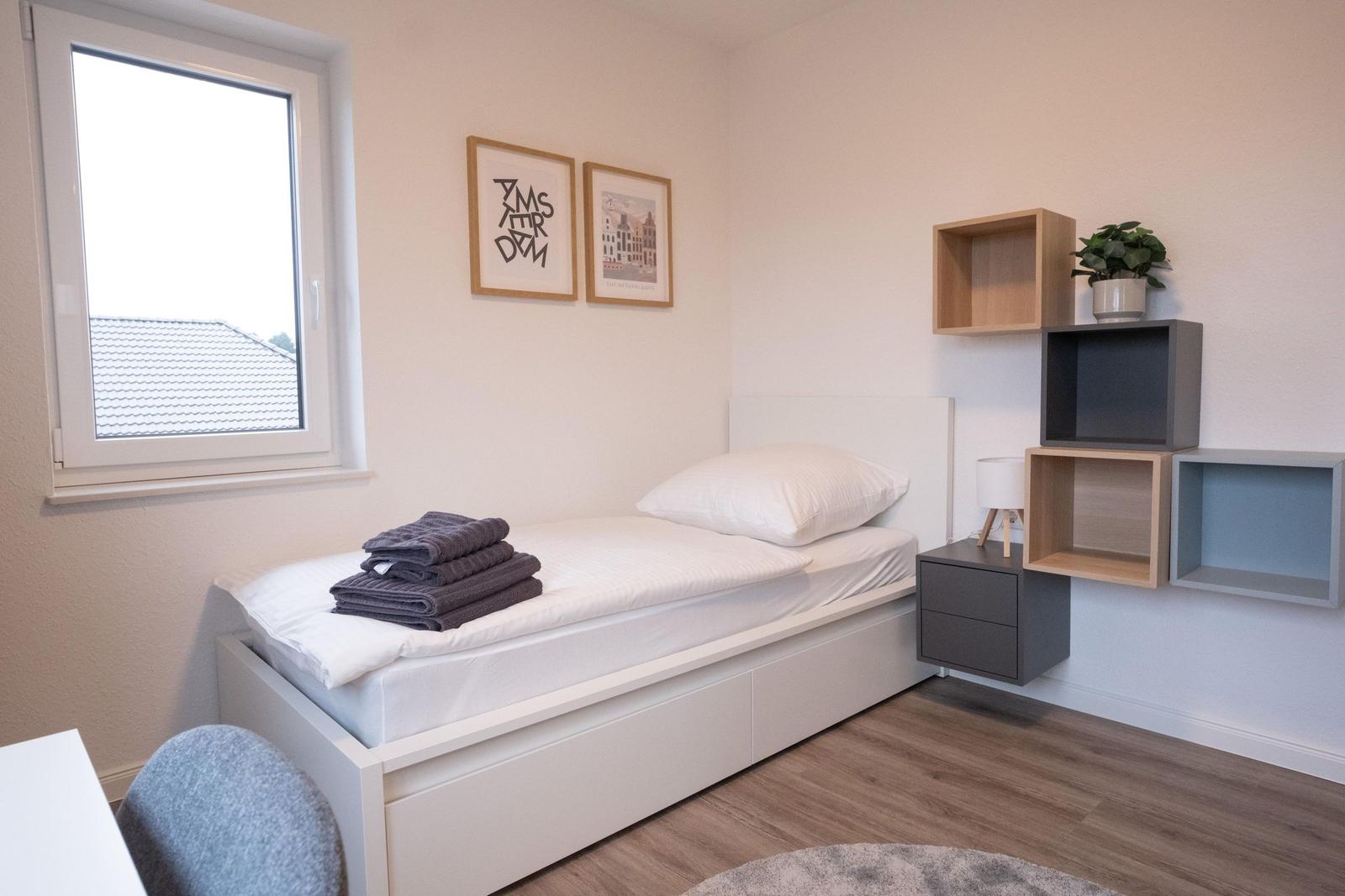 Ein Schlafzimmer mit Bett, Fenster und Wandregalen.