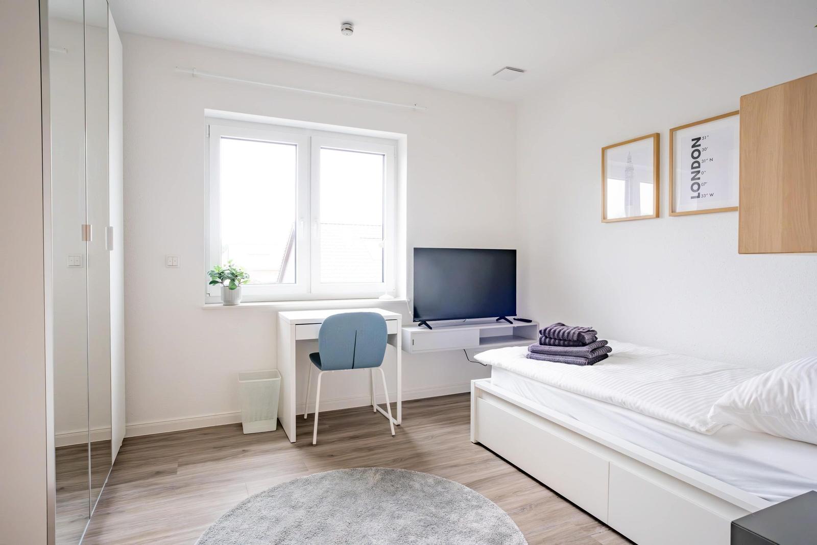 Schlafzimmer mit Bett, Schreibtisch, Fernseher und Kleiderschrank.