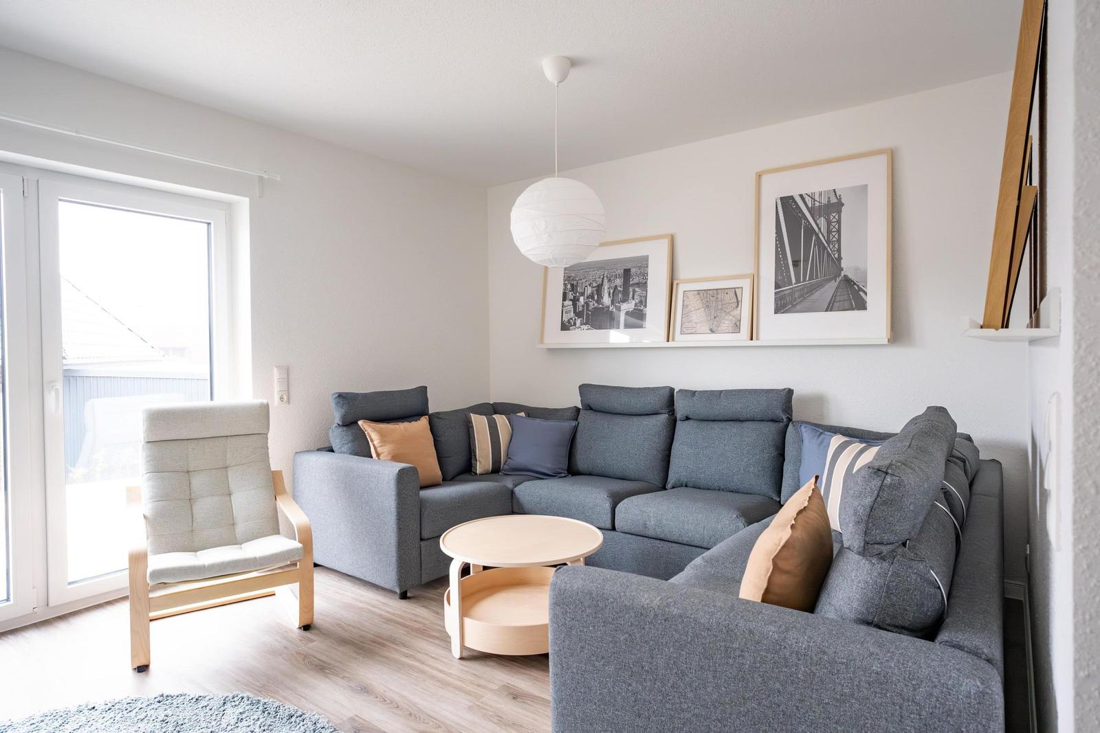 Wohnzimmer mit grauem Sofa, Holzstuhl und runden Tisch.