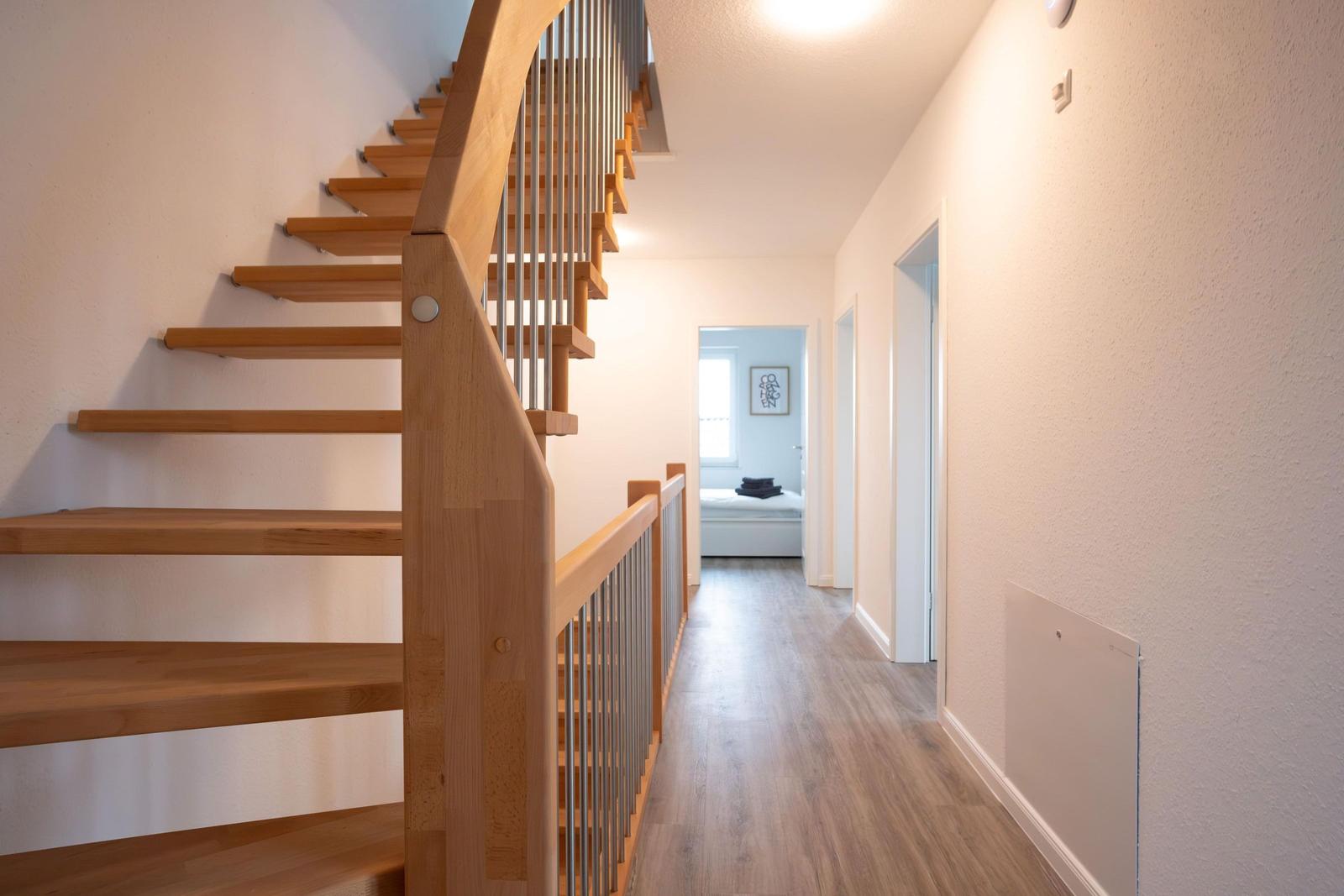 Holztreppe mit Metallgeländer führt zu einem Flur mit Holzboden und Türen zu Räumen.