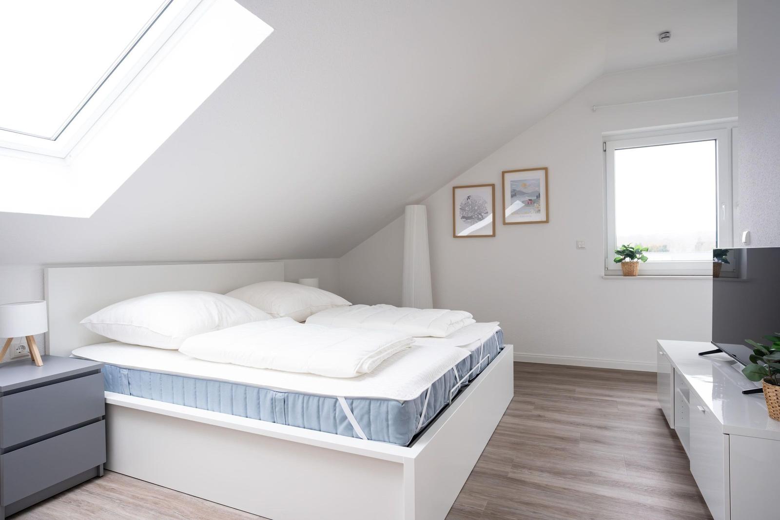 Schlafzimmer mit Dachschräge, Dachfenster, Bett und Schreibtisch.