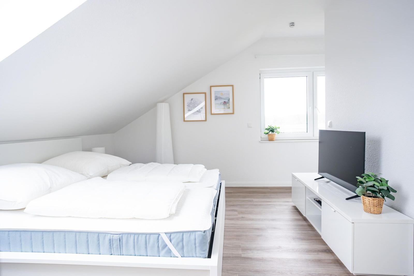 Schlafzimmer mit Dachbodenneigung, Bett, TV und Fenster.