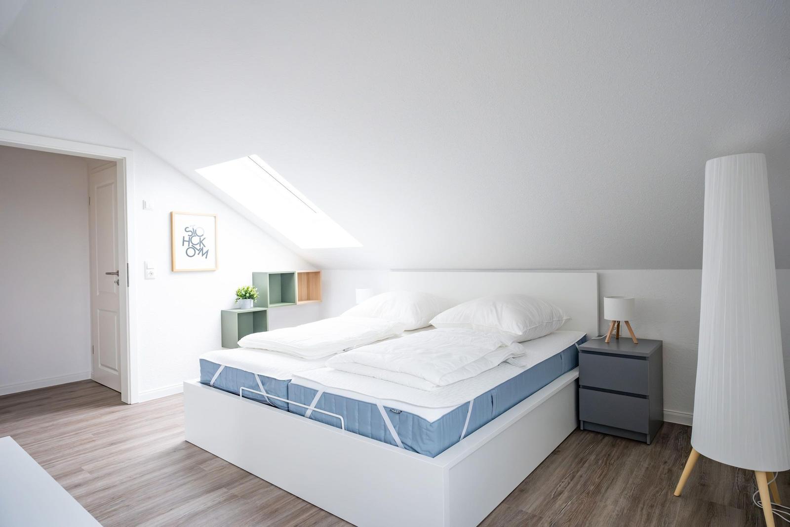 Schlafzimmer mit Dachschrägen, Doppelbett, Nachttisch und Stehlampe.