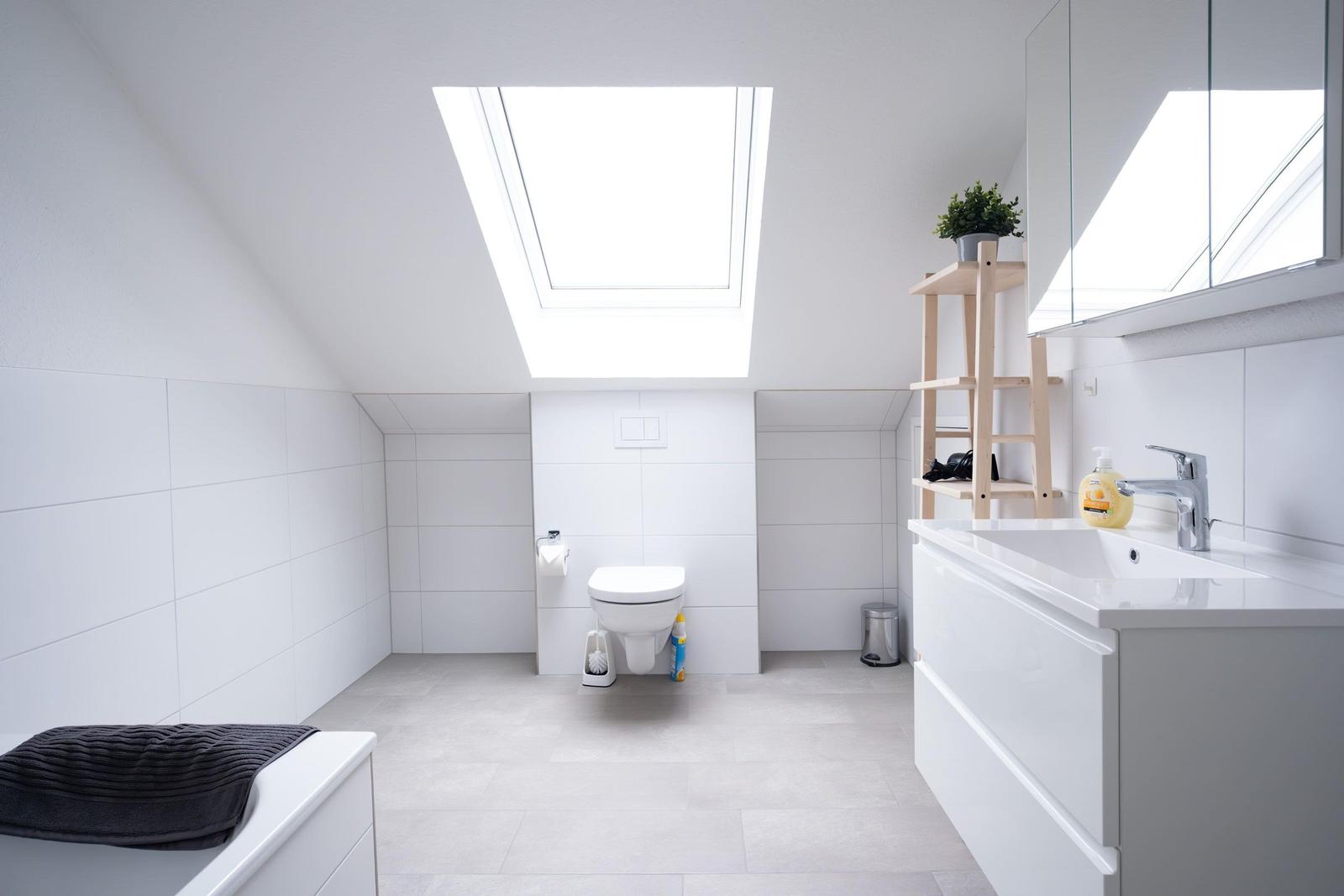 Badezimmer mit Dachfenster, Toilette, Waschbecken und Holzregal.