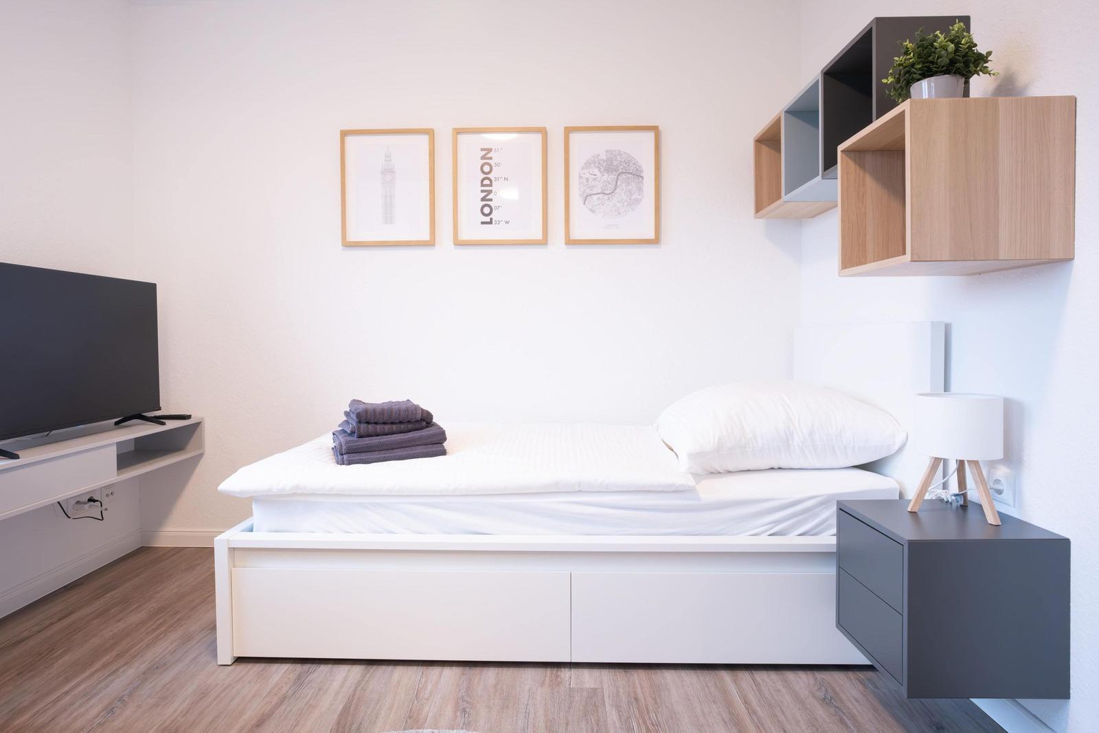 Schlafzimmer mit Bett, Fernseher und Wandregal.