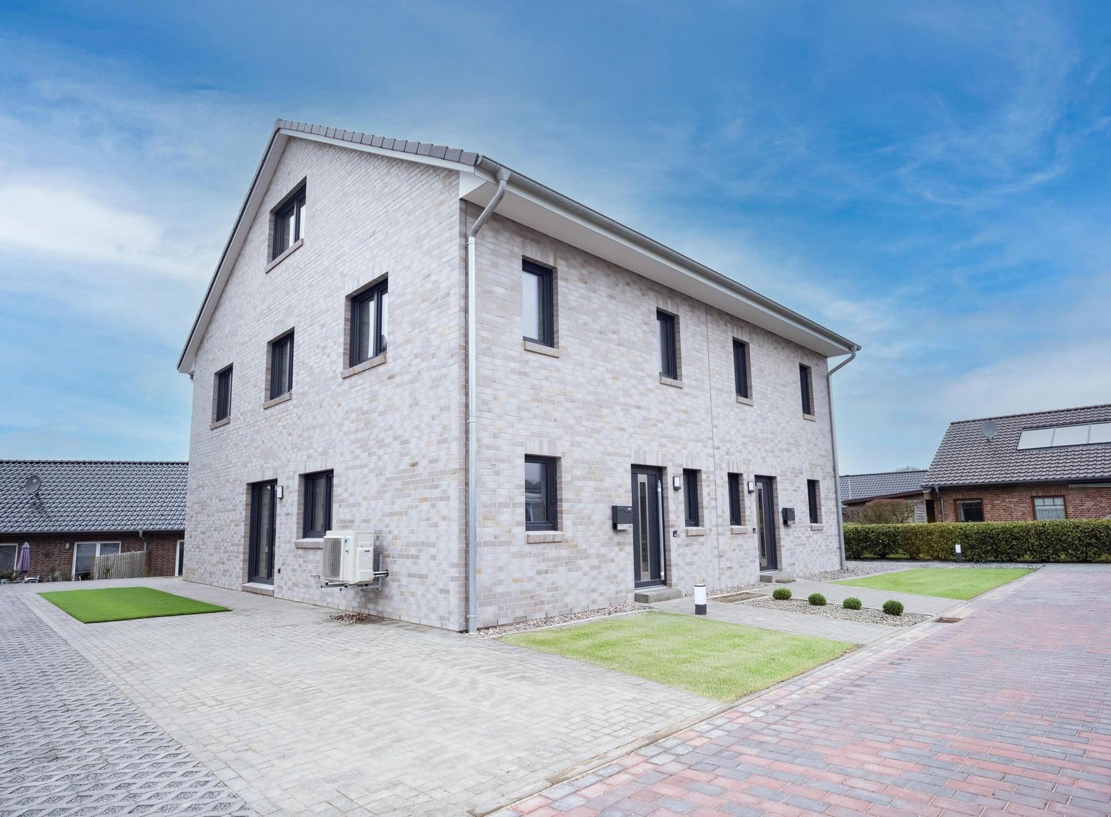 Modernes zweistöckiges Haus mit Steinmauer, Fenstern und Eingängen. Vorgarten mit Rasen und gepflastertem Weg.