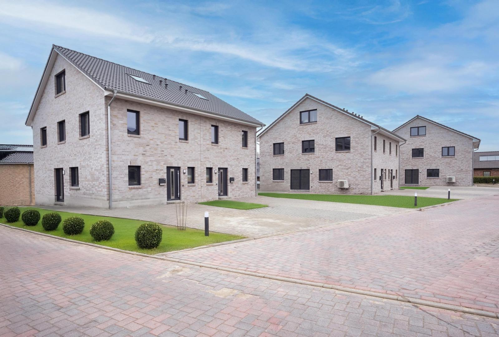 Drei moderne Wohnhäuser mit Steinfassade und Dachgauben.