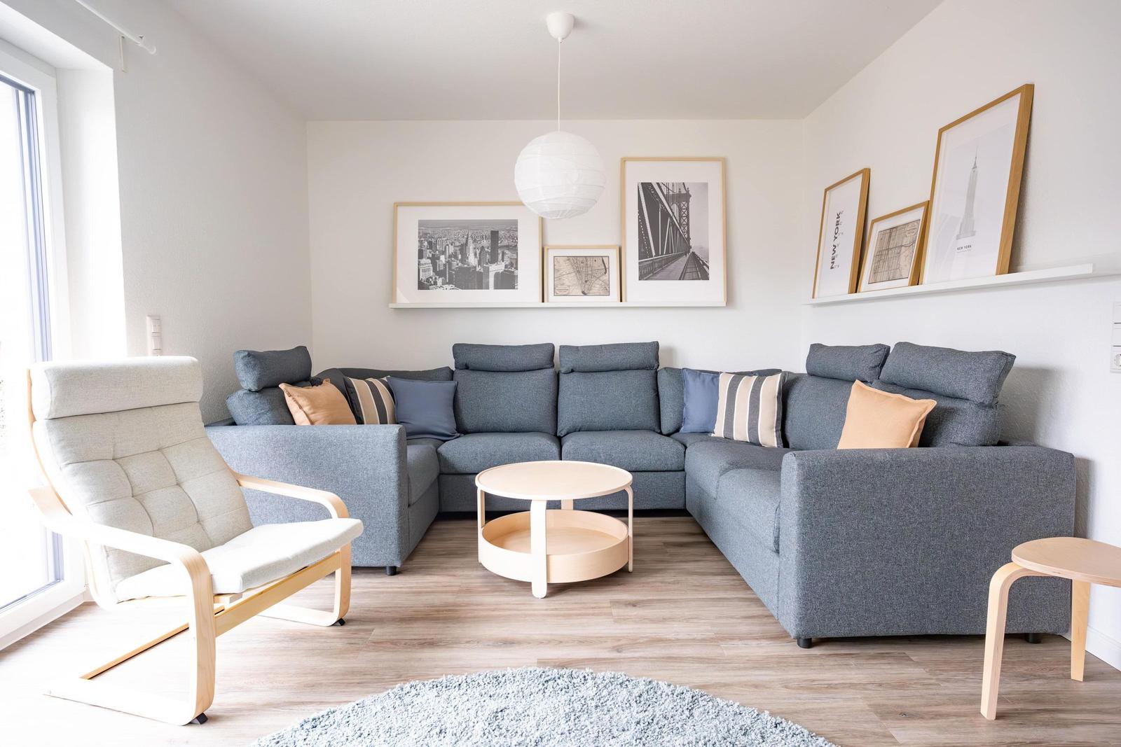 Ein Wohnzimmer mit grauem Sofa, Holzmöbeln und Wandbildern.