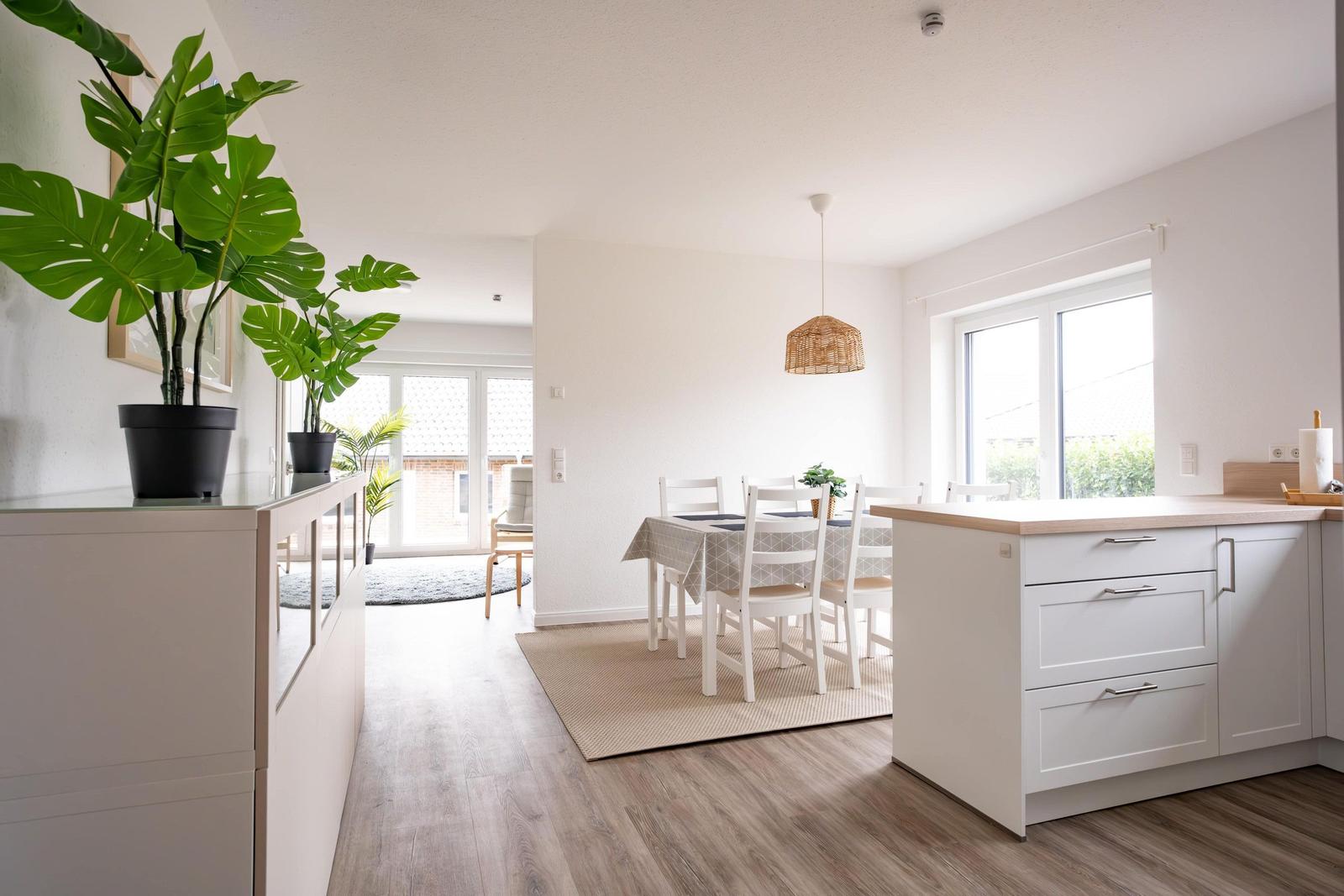 Küche mit Essbereich, weiße Möbel, Holzboden und große Fenster.