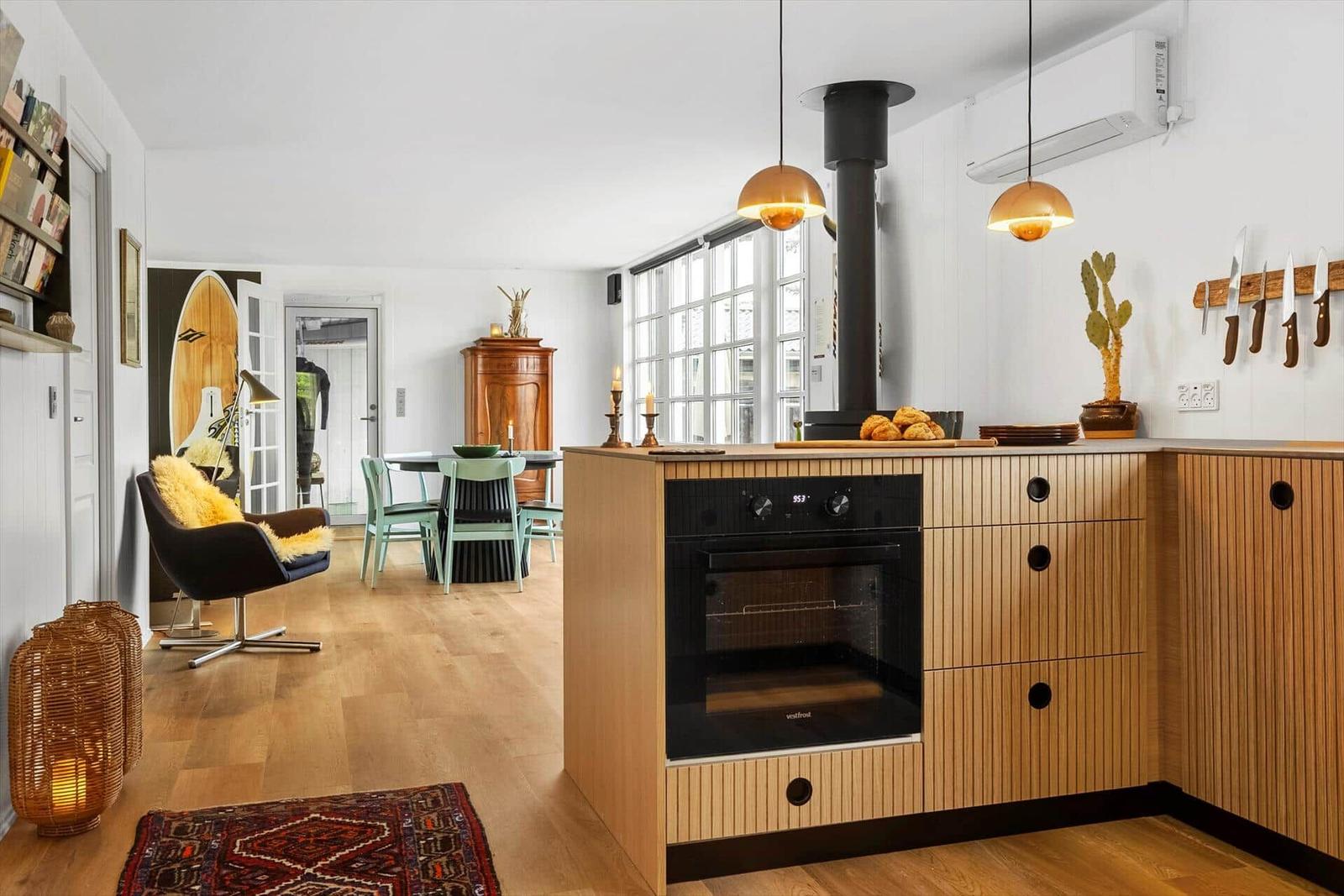 Küche mit Holzschrank, Ofen und Kücheninsel. Im Hintergrund Essbereich und Wohnzimmer.