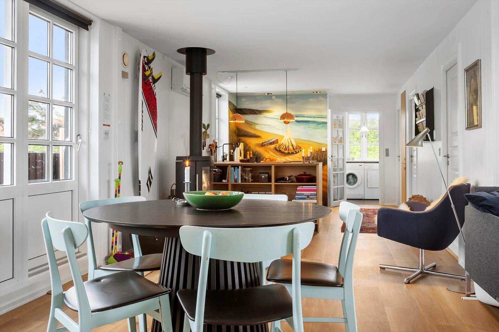 Essbereich mit runder Tisch und Stühlen, Kamin und Wandbild im Hintergrund.