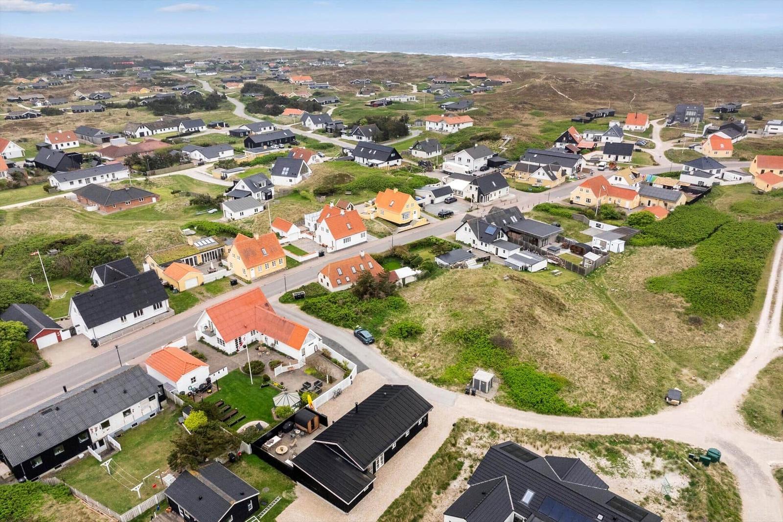 Aerial view of a coastal village with houses, roads, and the sea in the background.