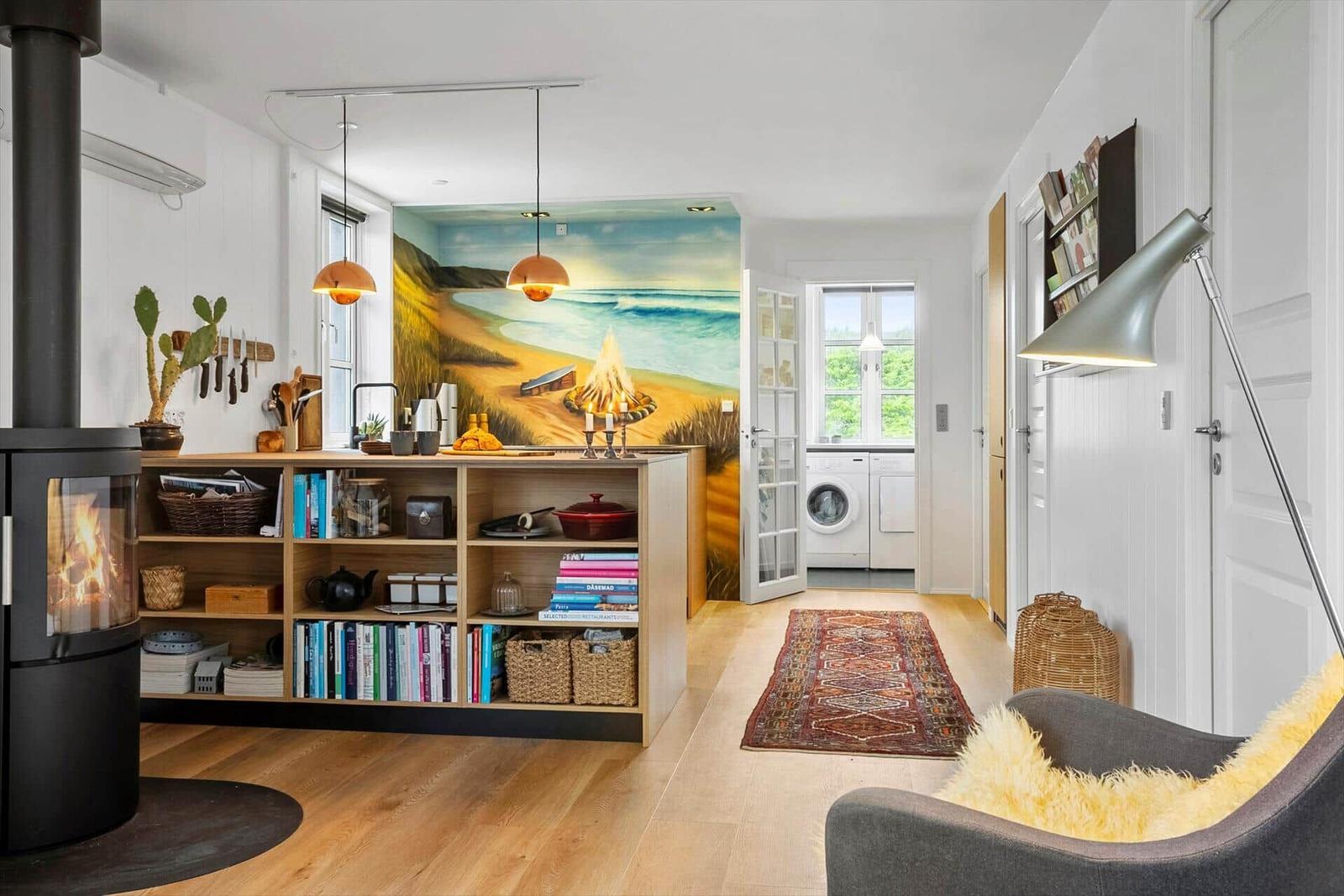 Wohnbereich mit Kamin, Küchenzeile und Wandbild. Flur mit Waschmaschine und Teppich.