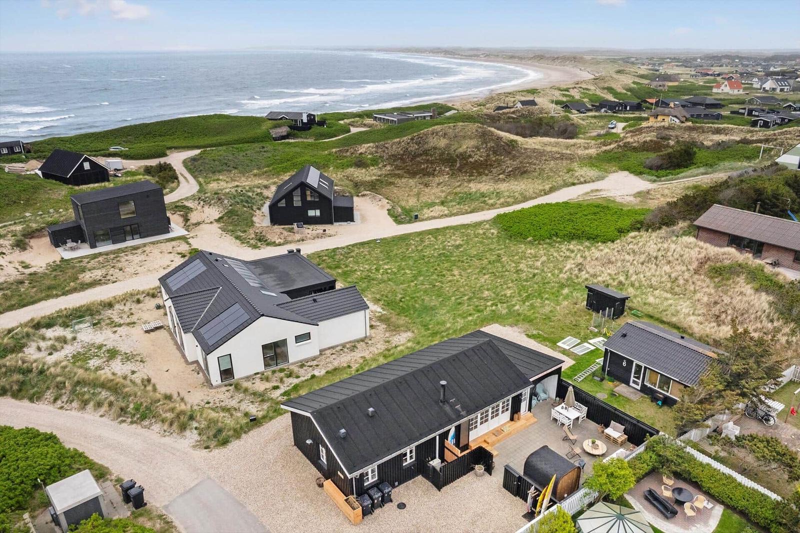 Moderne Strandhäuser mit Terrassen und Garten, umgeben von Dünen und Meeresblick.