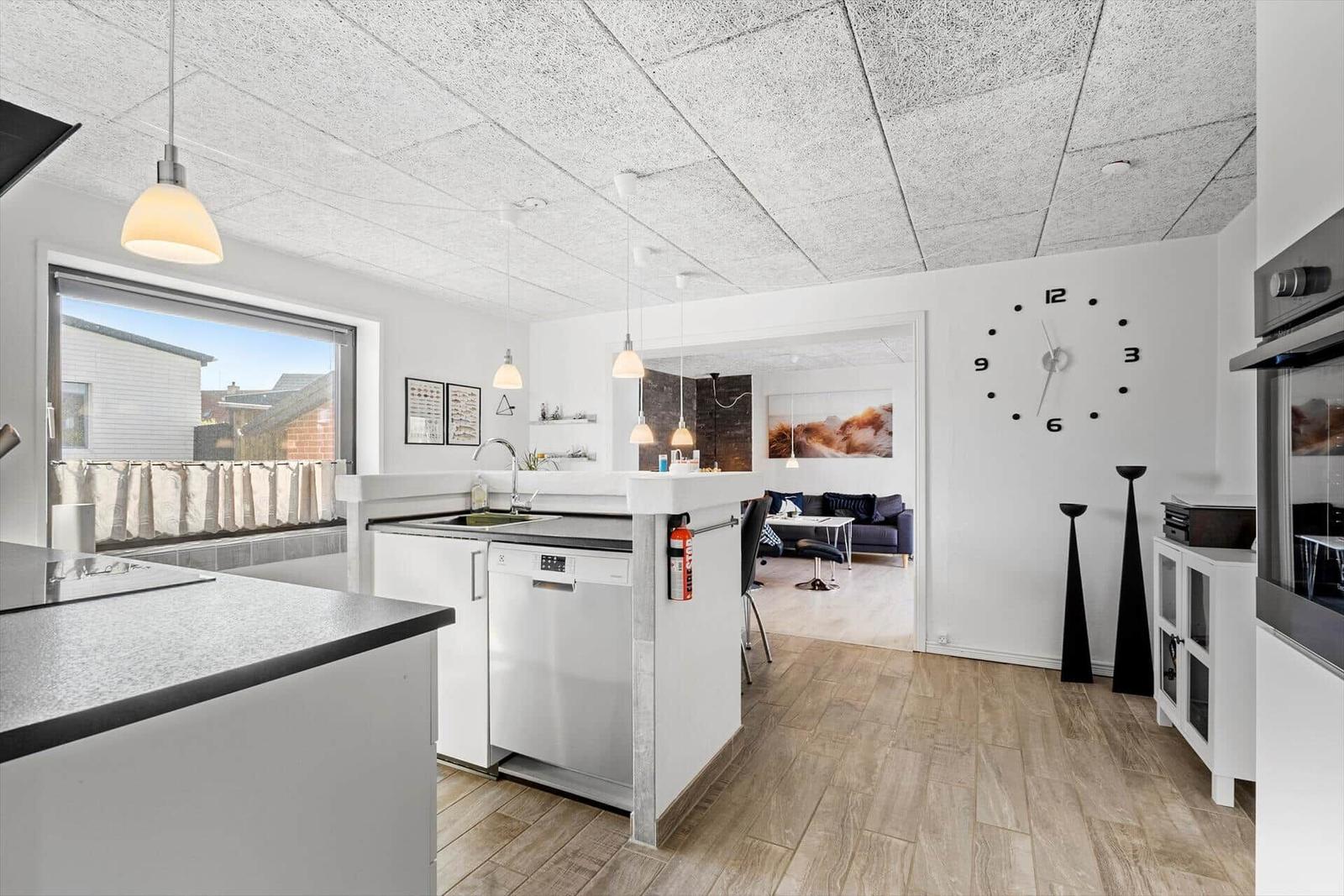 Küche mit Essbereich und Wohnzimmer im Hintergrund. Große Fenster und moderne Einrichtung.