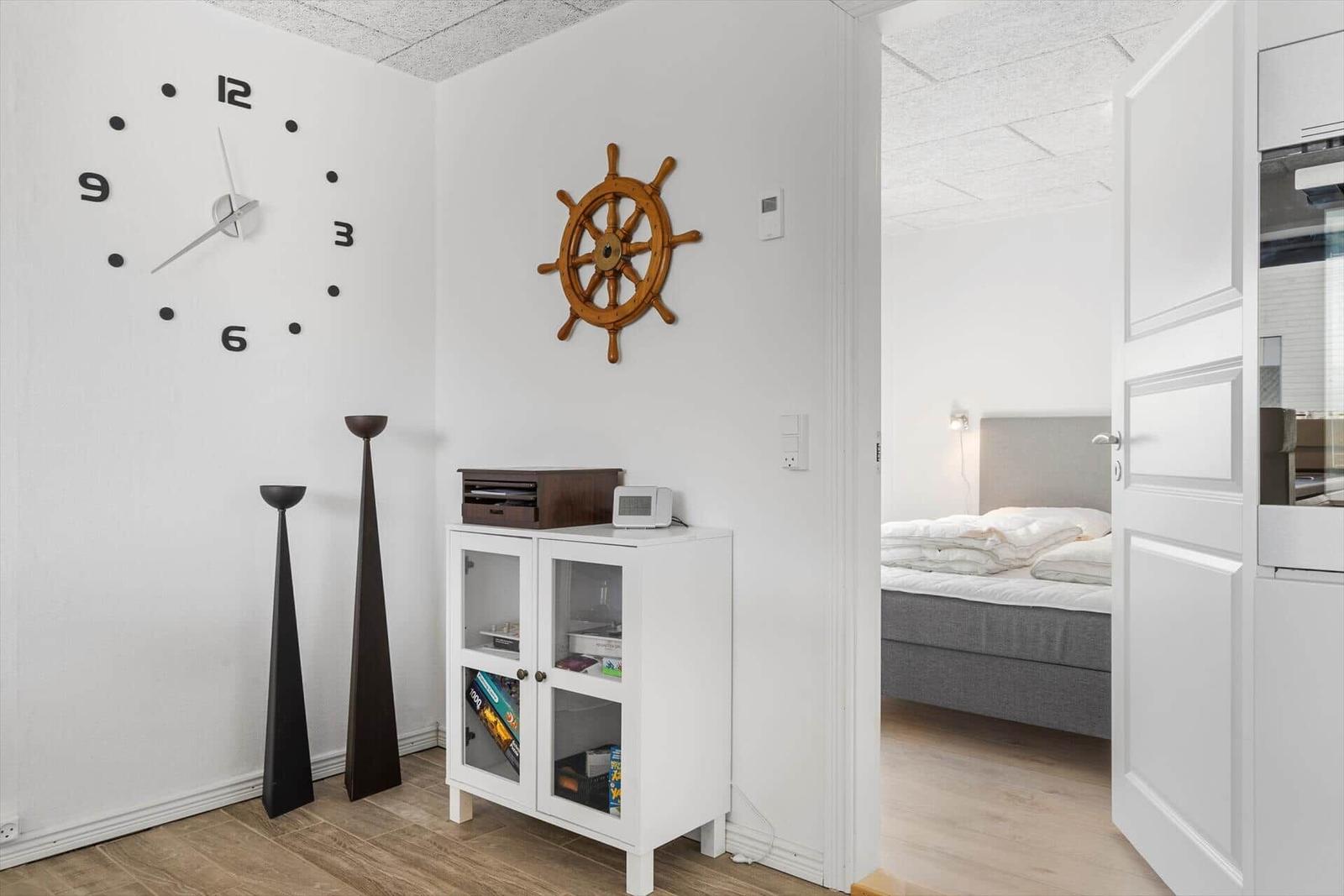 Raum mit Wanduhr, Steuerrad und Schrank. Durchgang zu Schlafzimmer mit Bett.