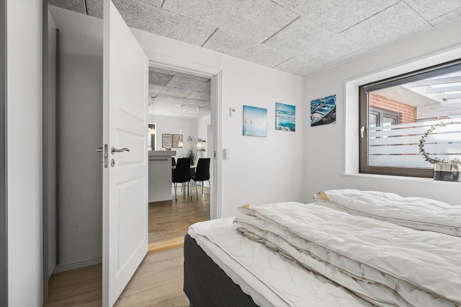 Schlafzimmer mit Blick in Wohnbereich und Fenster mit Blick auf Außenbereich.