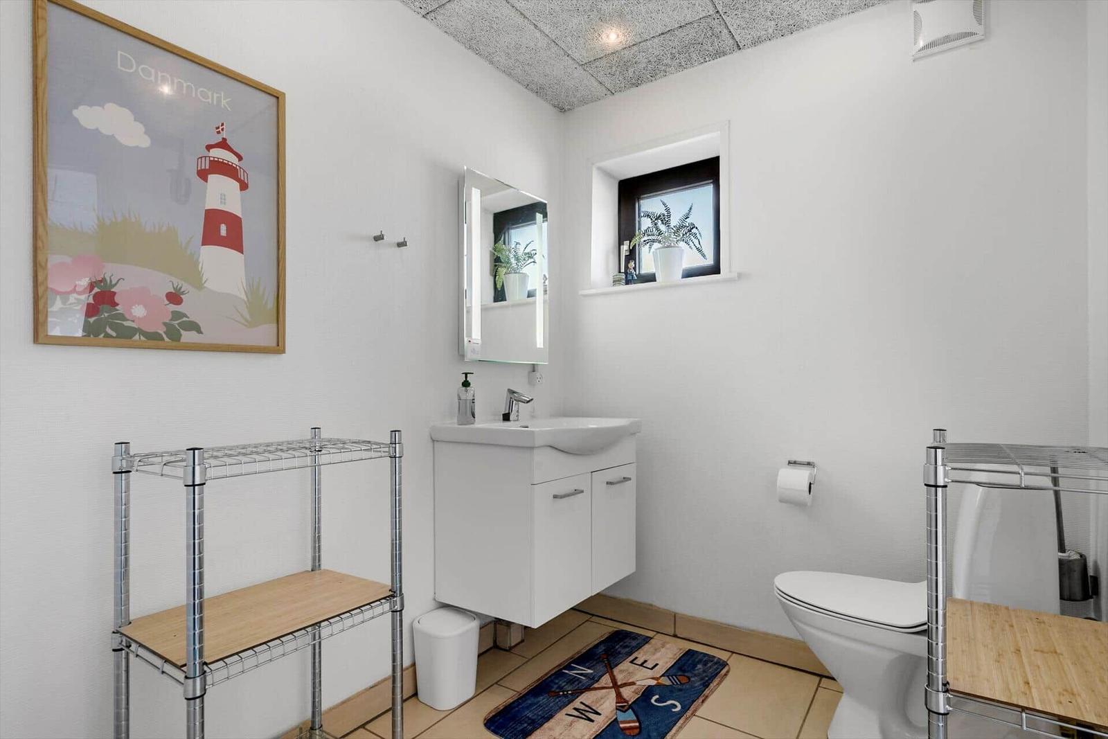 Badezimmer mit Waschbecken, Toilette und Fenster mit Pflanze.