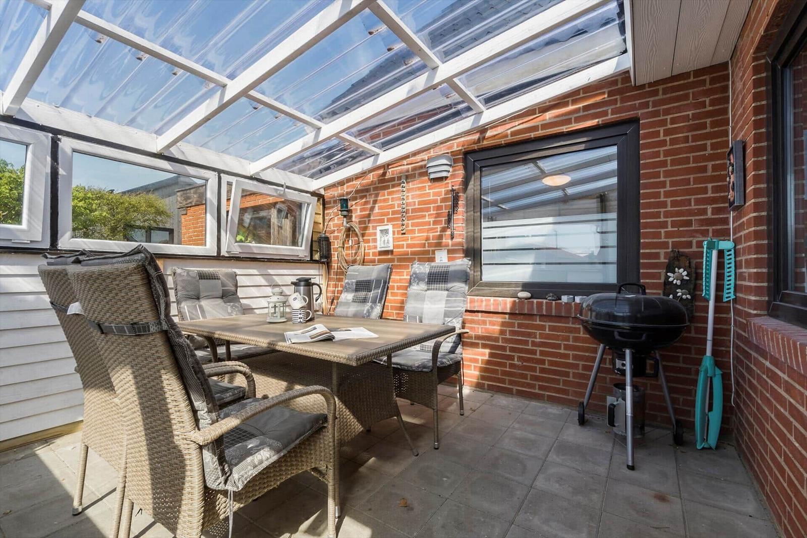 Gartenbereich mit Sitzgruppe, Grill und Glasdach.