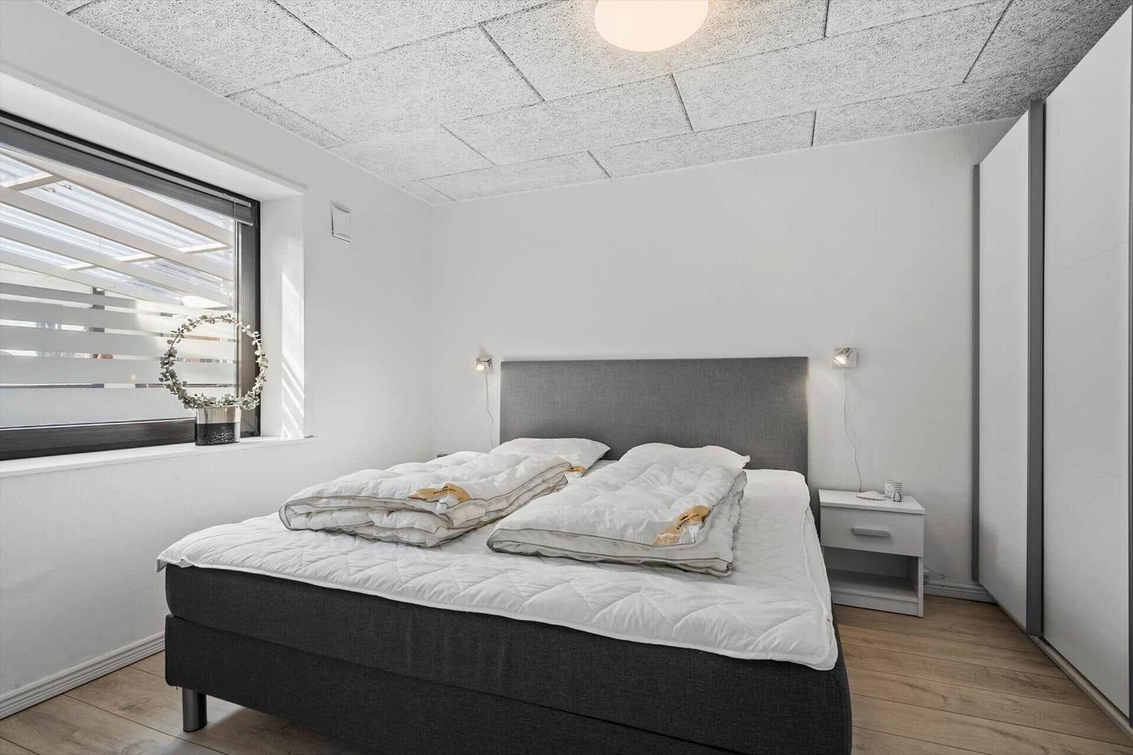 Schlafzimmer mit Doppelbett, Nachttisch und Fenster mit Jalousie.