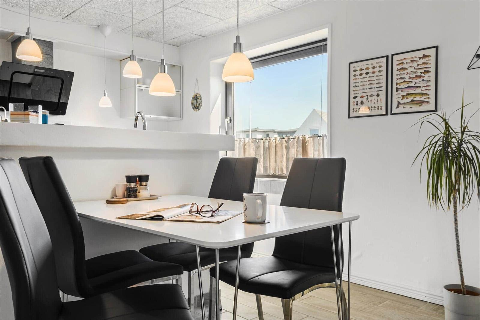 Essbereich mit Tisch, Stühlen und Fensterblick. Wandbilder und Pflanze sichtbar.