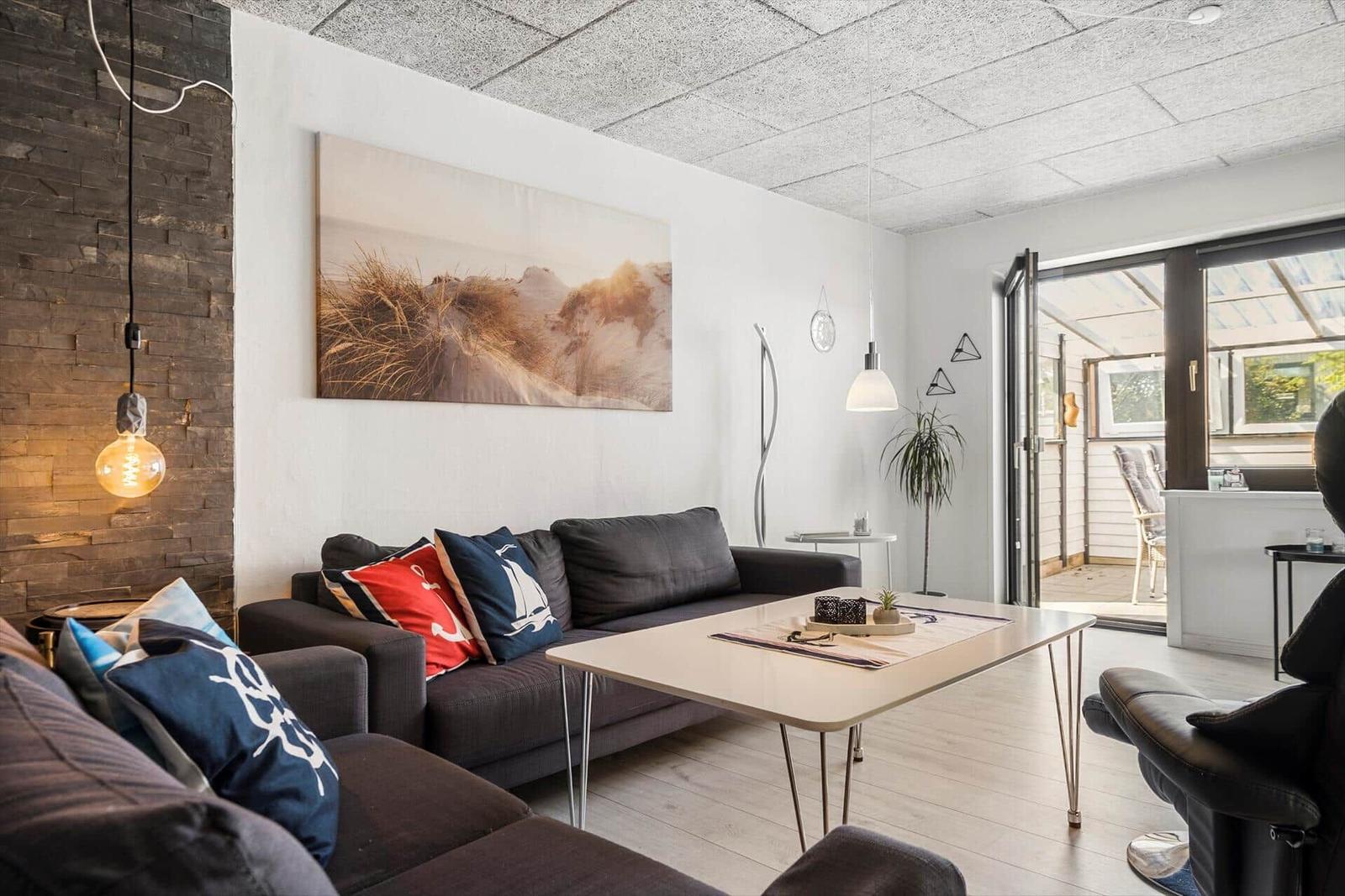 Wohnzimmer mit Sofa, Tisch und Wandbild. Durchgang zur Terrasse.