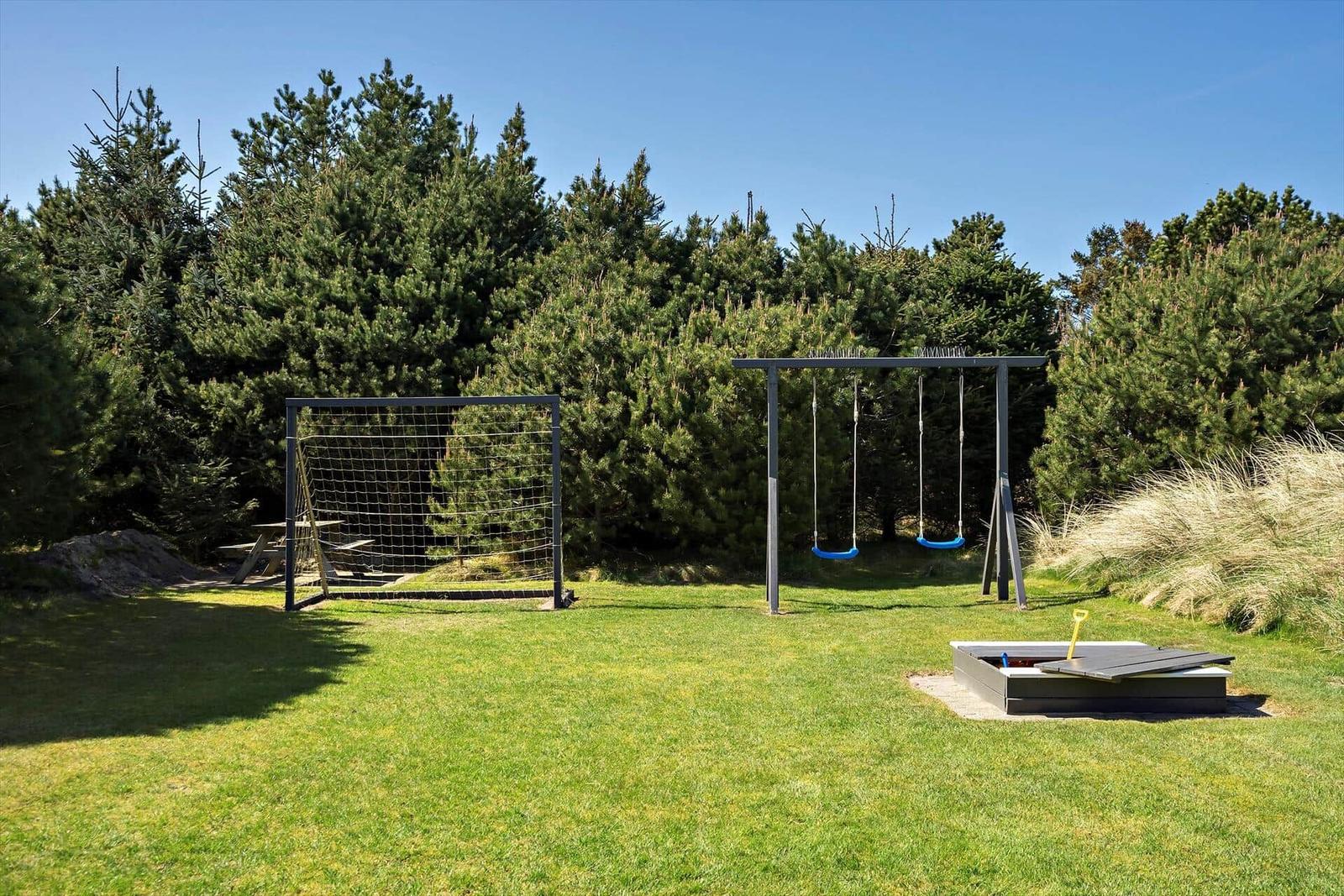 Grüner Garten mit Spielplatz, Schaukel und Sandkasten vor Bäumen.
