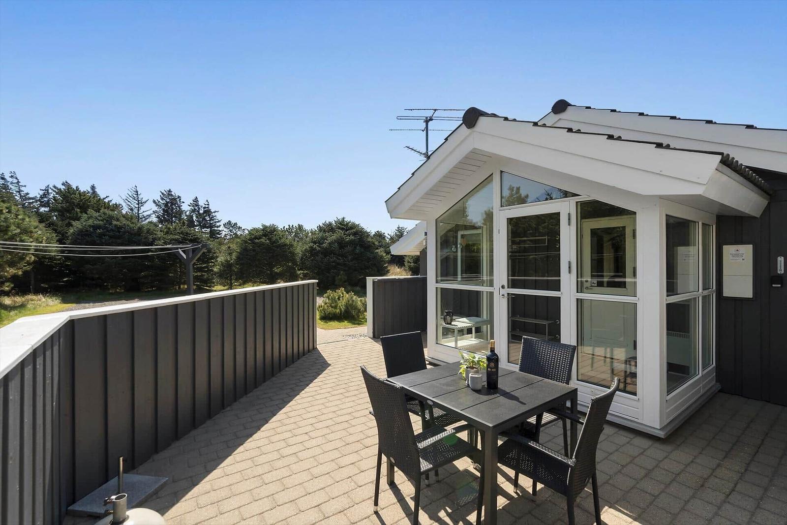 Terrasse mit Sitzgruppe vor modernem Haus mit Glasfront und Waldblick.
