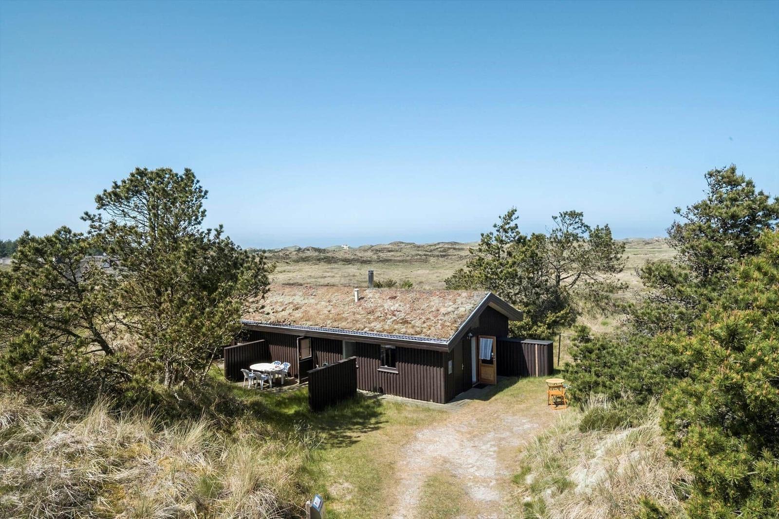 Holzhaus mit Terrasse und Grillplatz in einer grünen Umgebung mit Blick auf die Landschaft.