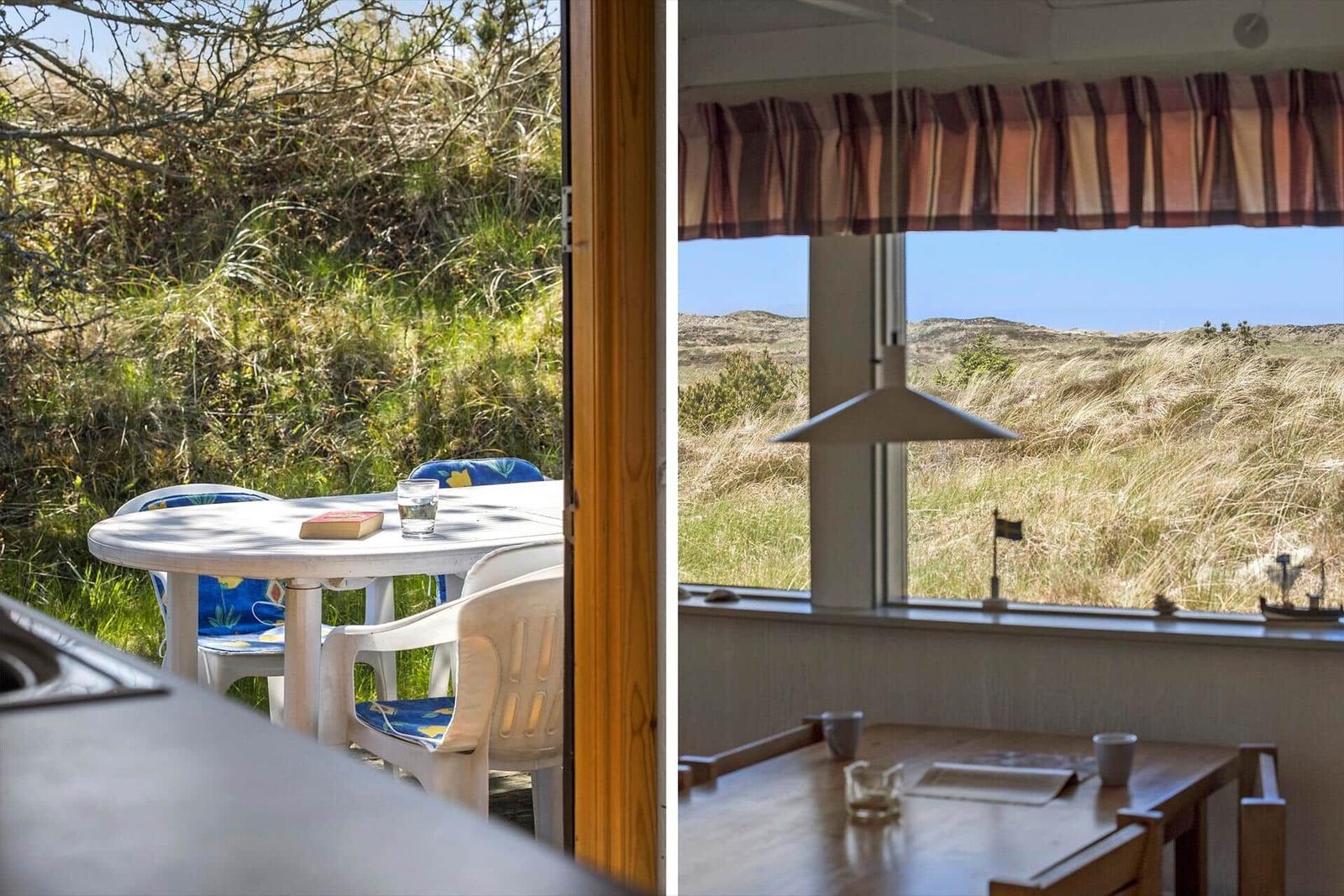 Terrasse mit Tisch und Stühlen. Blick auf Dünen und Himmel durch Fenster.