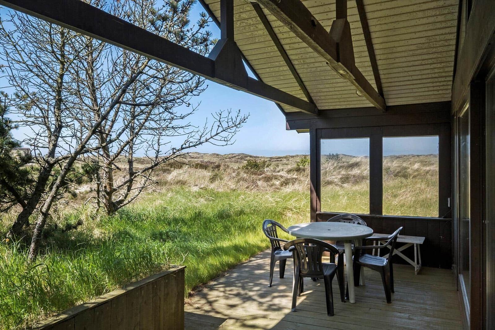 Terrasse mit Tisch und Stühlen, Blick auf Gras und Bäume.
