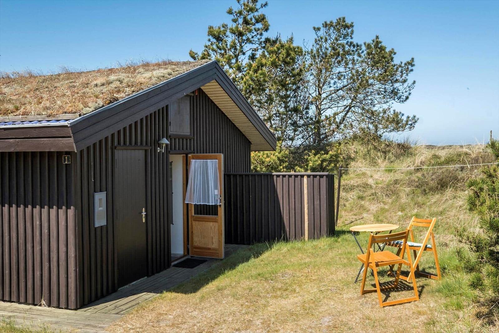 Holzhaus mit Grasdach, Terrasse und Gartenmöbel in natürlicher Umgebung.