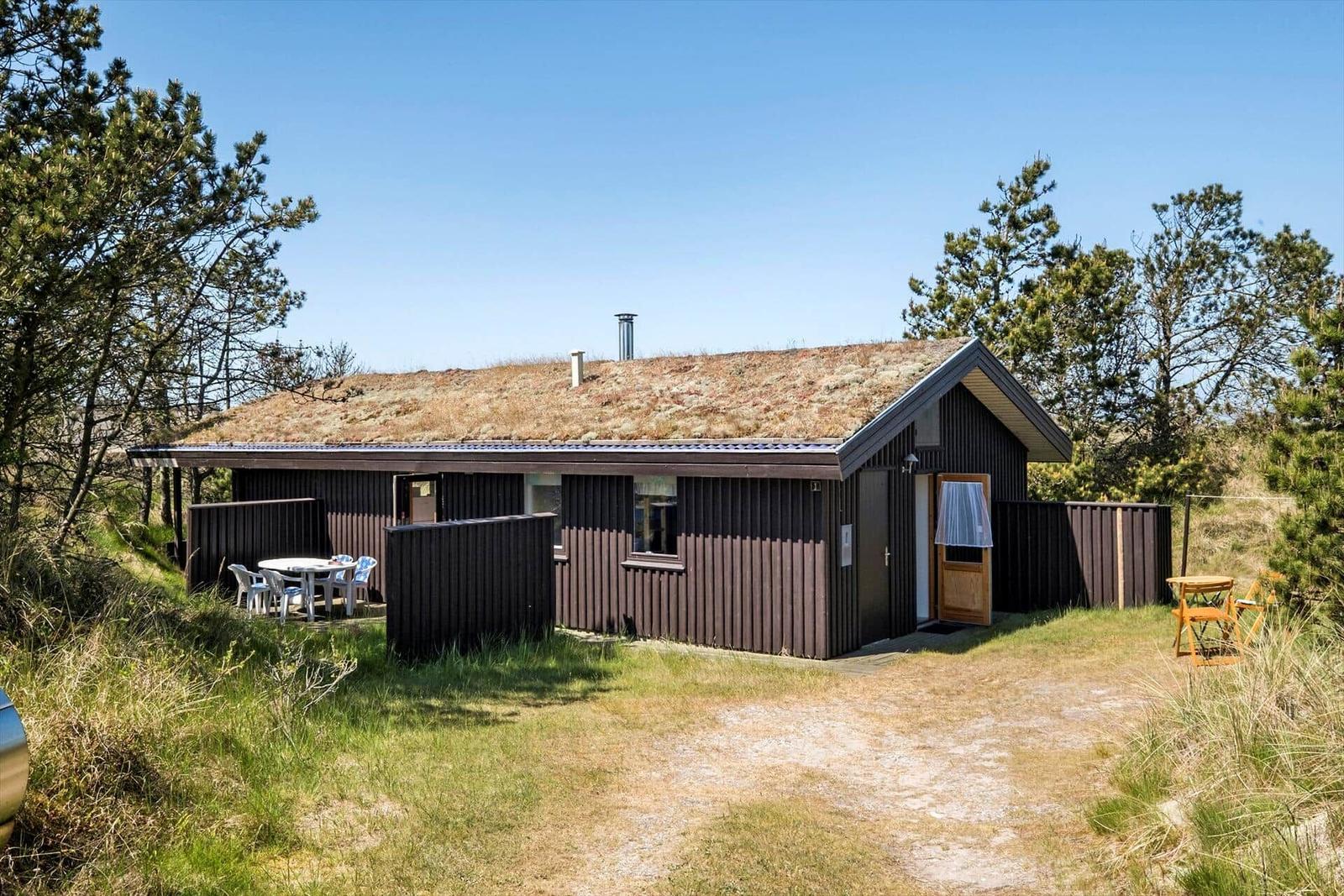 Holzhütte mit Grasdach, Terrasse und Garten. Tisch und Stühle im Freien.