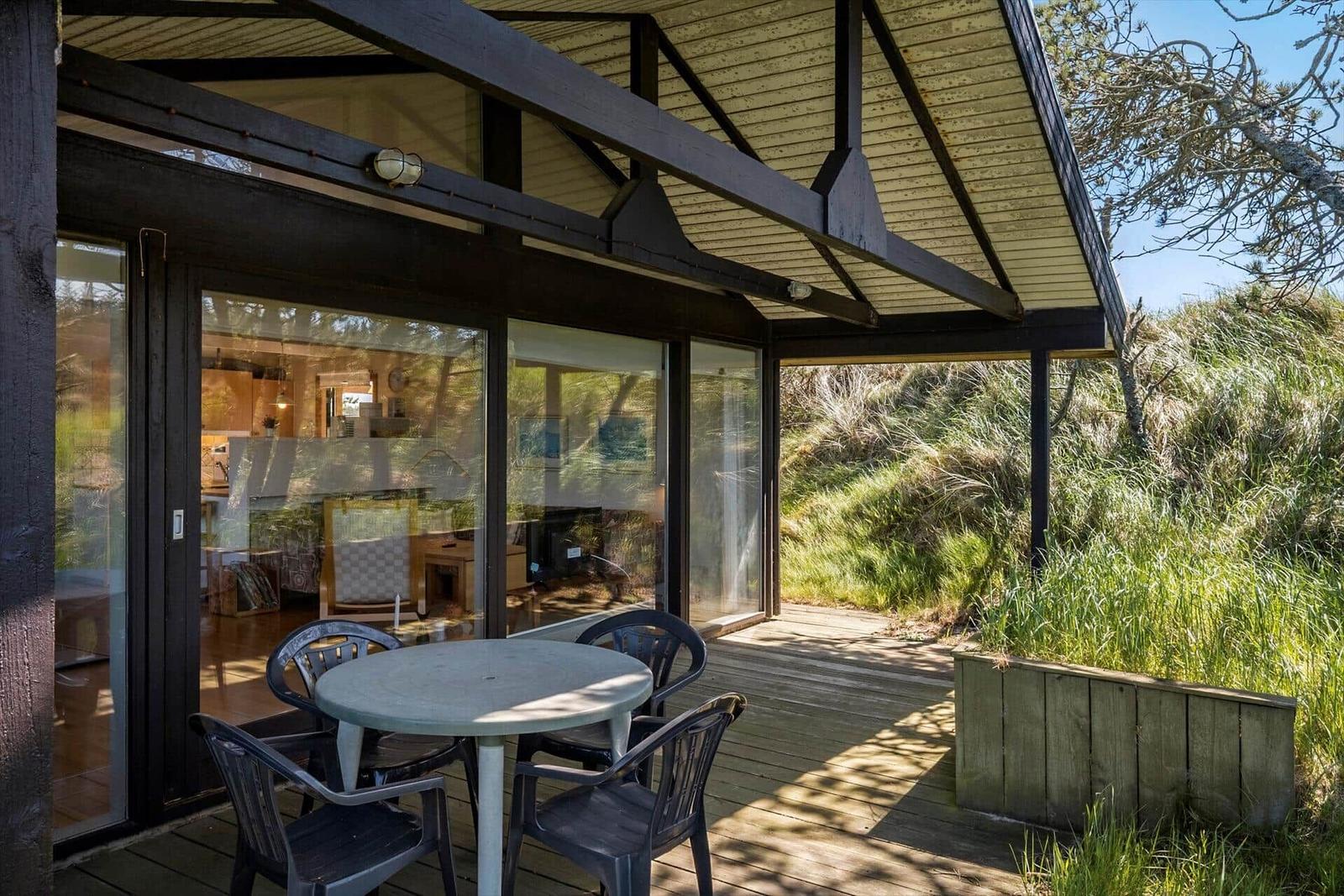 Terrasse mit Tisch und Stühlen, Blick in Wohnbereich, umgeben von Grünflächen.