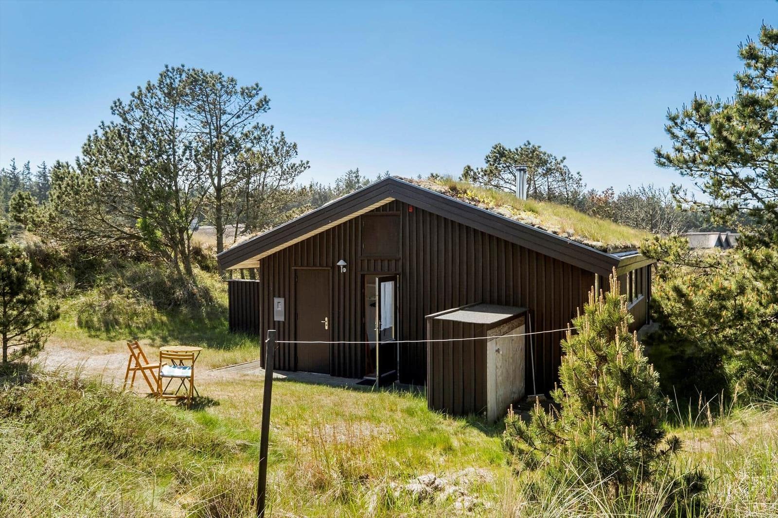 Holzhaus mit grüner Dachbegrünung, Außentisch und Stühle im Gras.