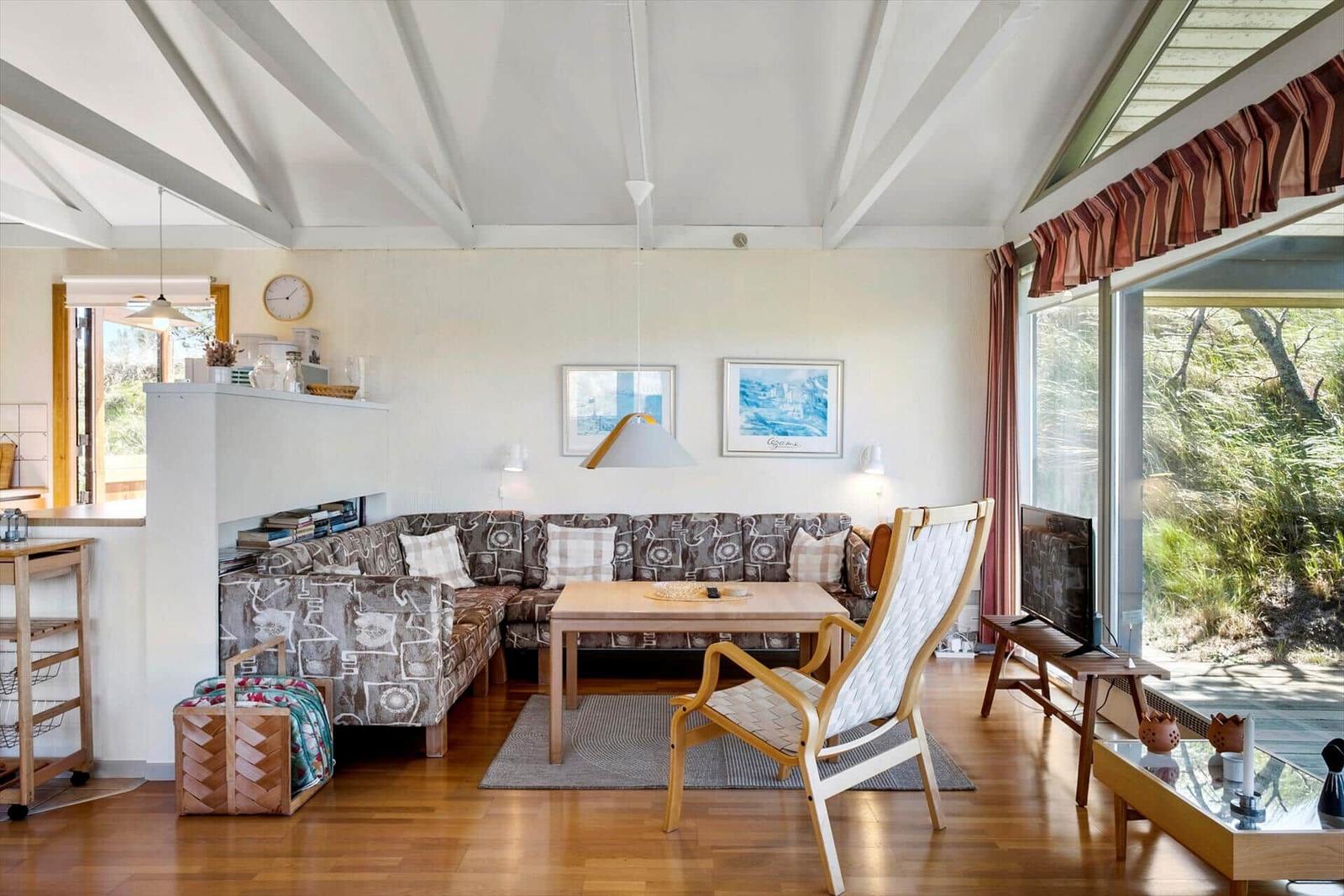 Wohnzimmer mit Sofa, Stuhl und TV. Große Fenster und Holzboden.