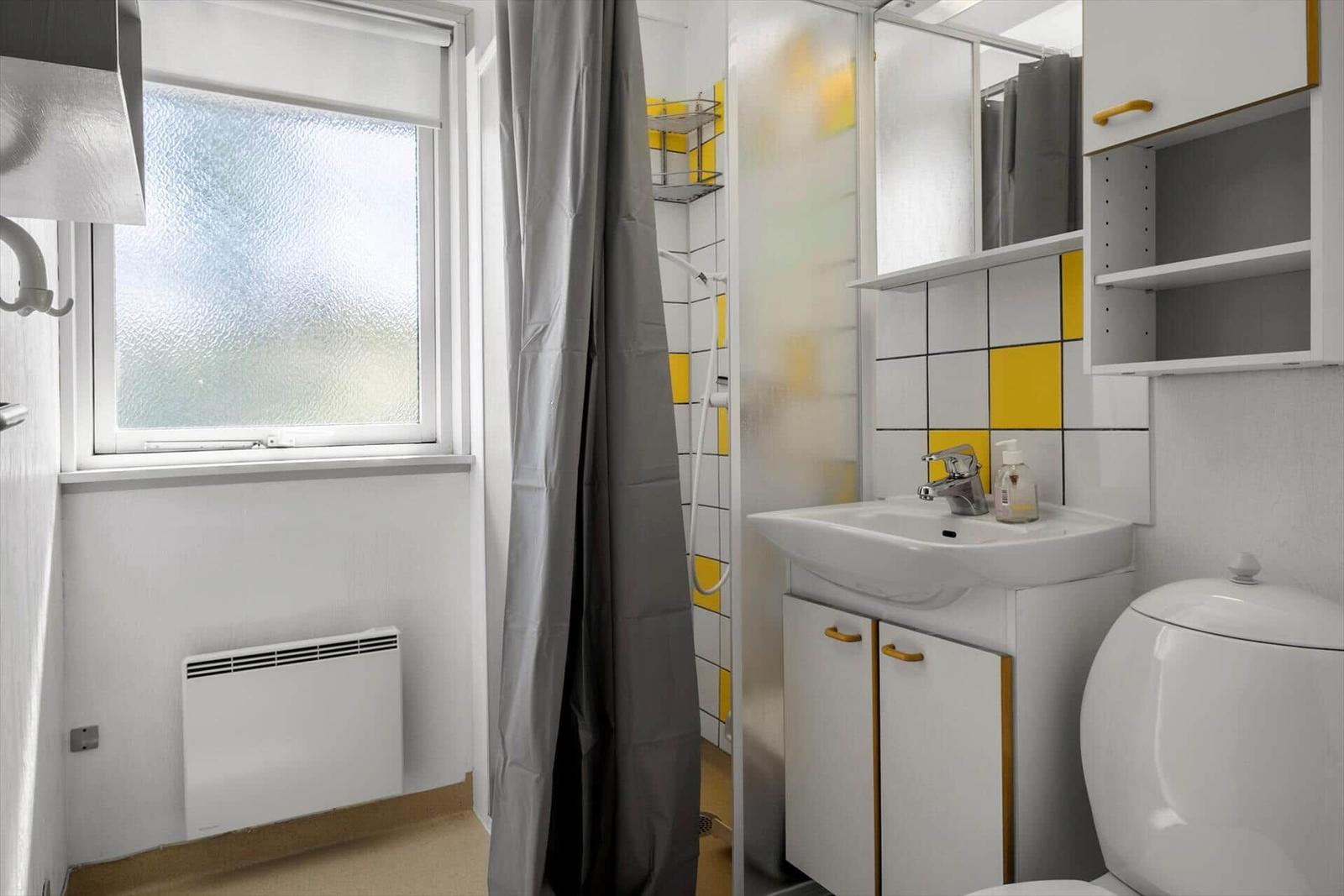 Badezimmer mit Dusche, Waschbecken und Toilette. Gelbe Fliesen und graue Vorhänge.