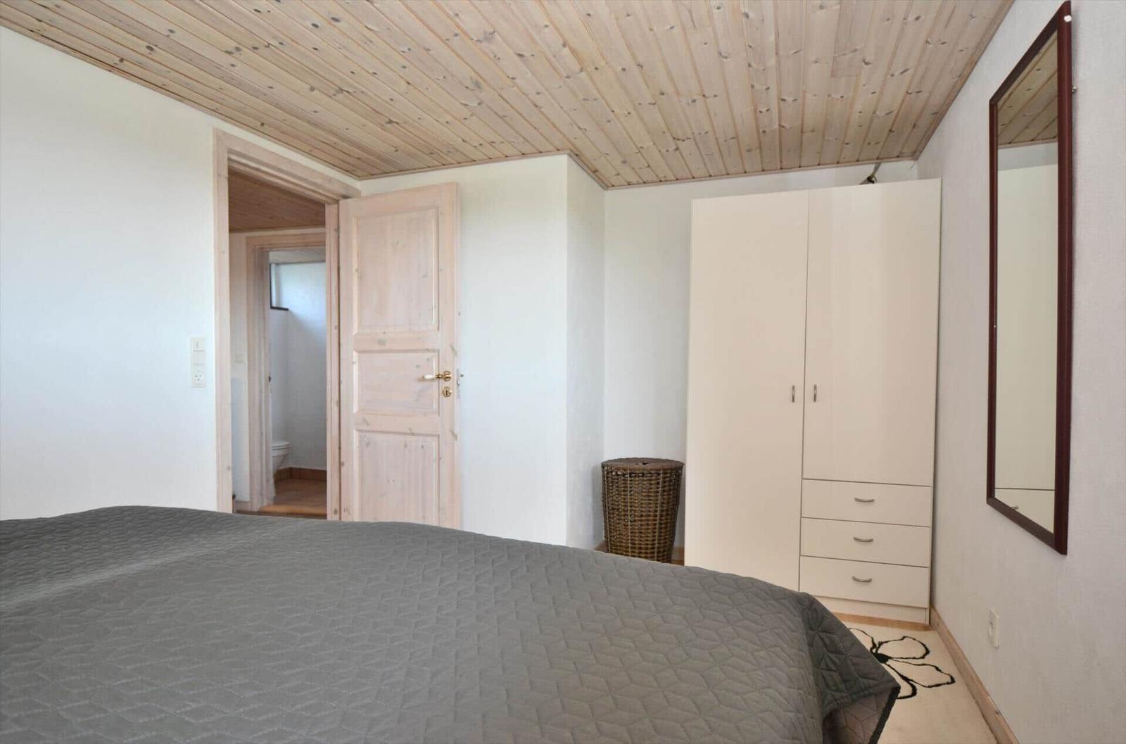 Schlafzimmer mit Bett, Kleiderschrank und Spiegel. Holzdecke und Tür sichtbar.