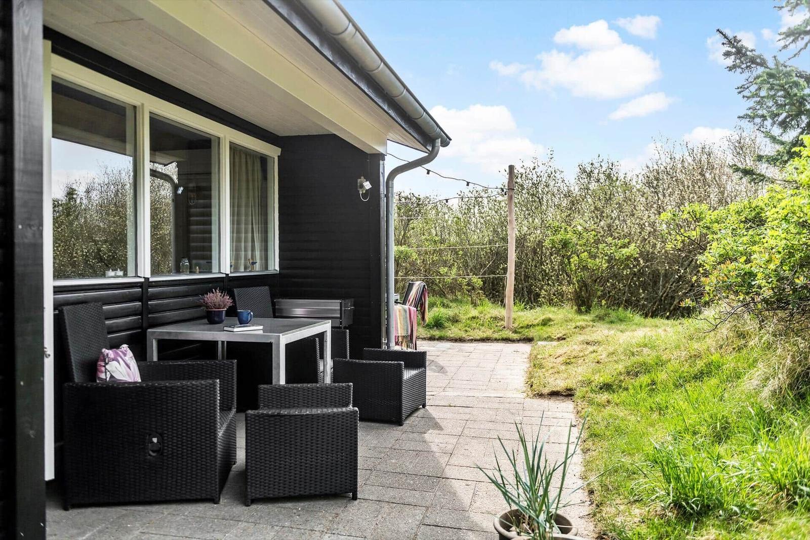 Terrasse mit Sitzgruppe, Grill und Blick auf Grünflächen.